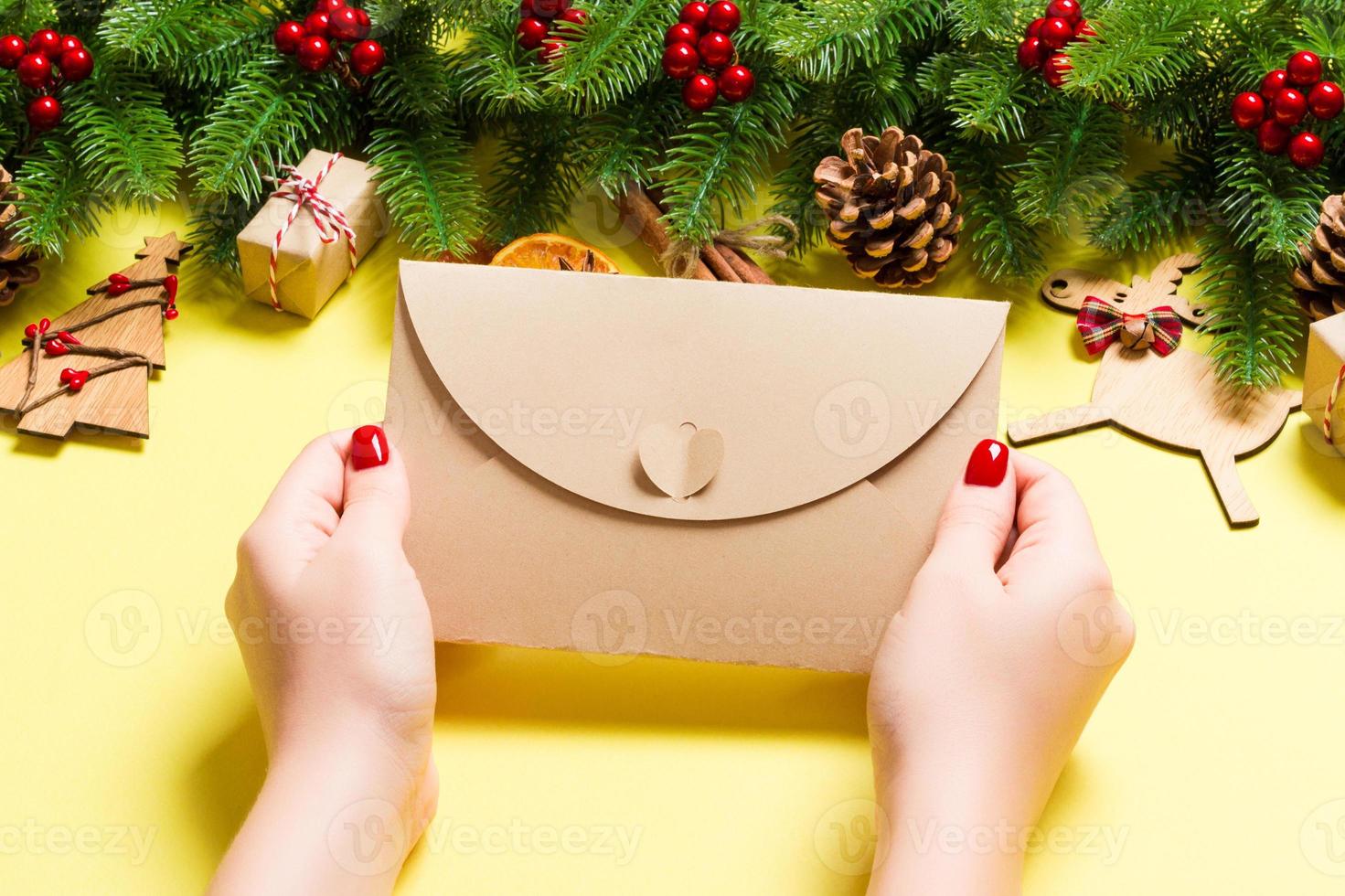 Top view of woman holding an envelope on yellow background made of holiday decorations. Christmas time concept photo