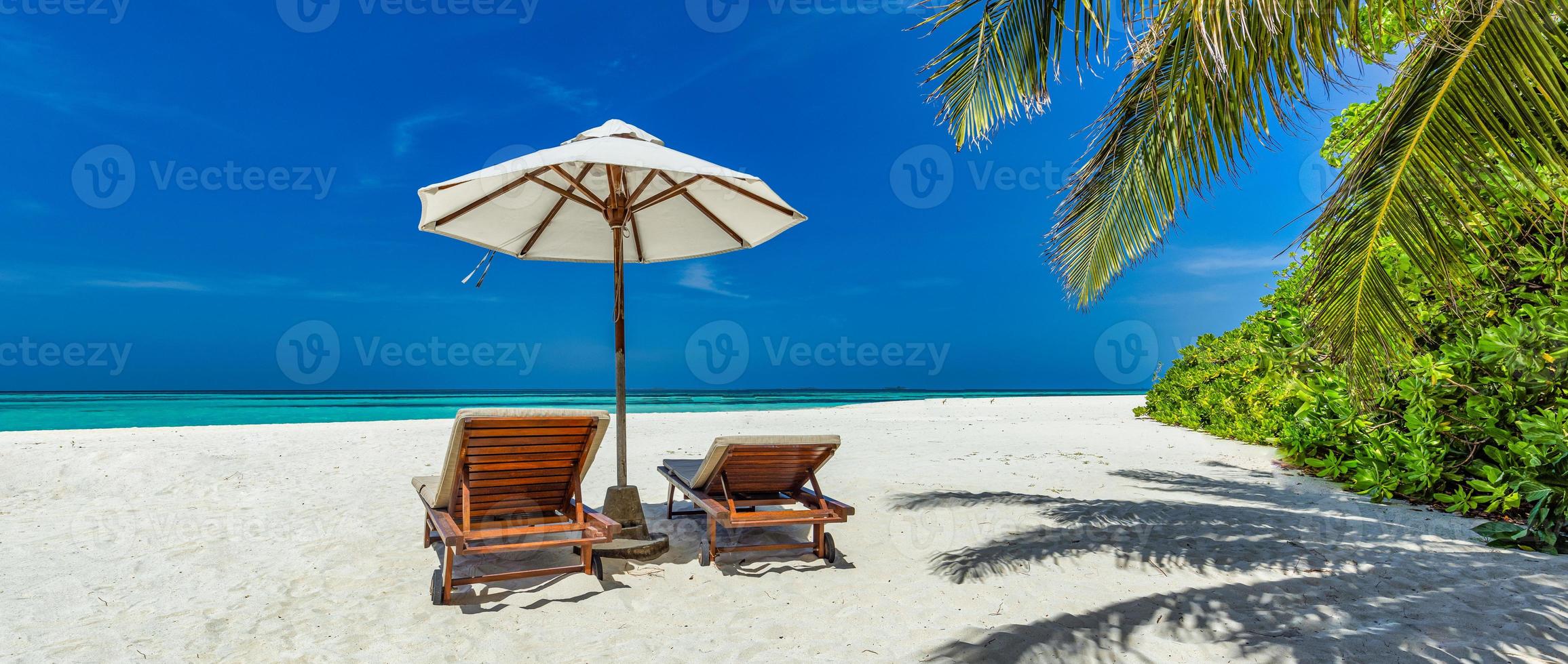 Beautiful tropical sunny shore, couple sun beds chairs umbrella under palm tree leaves. Sea sand sky. Romantic relax lifestyle panoramic island beach background. Summer travel exotic vacation panorama photo