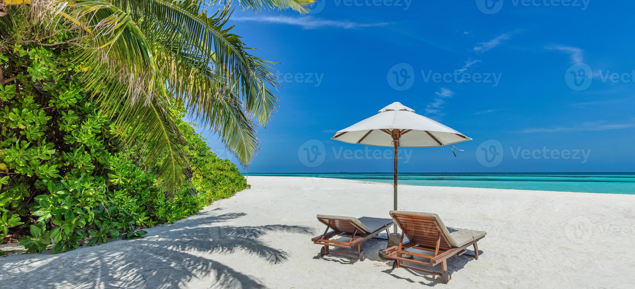 Beautiful tropical sunny shore, couple sun beds chairs umbrella under palm tree leaves. Sea sand sky. Romantic relax lifestyle panoramic island beach background. Summer travel exotic vacation panorama photo