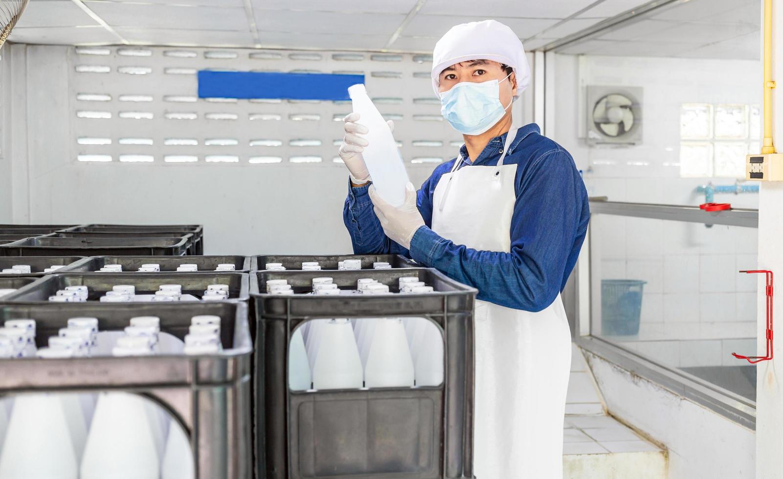 Young man worker or quality inspector in workwear and with a protective mask on his face working in checking bottled drinking water in drink water factory before shipment.drinking water business photo