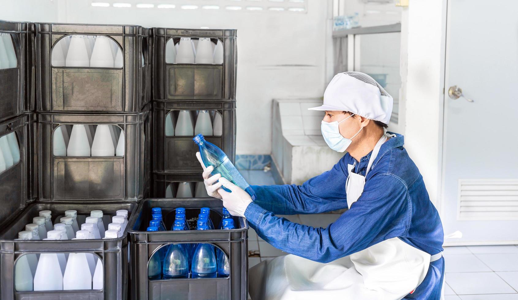 Young man worker or quality inspector in workwear and with a protective mask on his face working in checking bottled drinking water in drink water factory before shipment.drinking water business photo