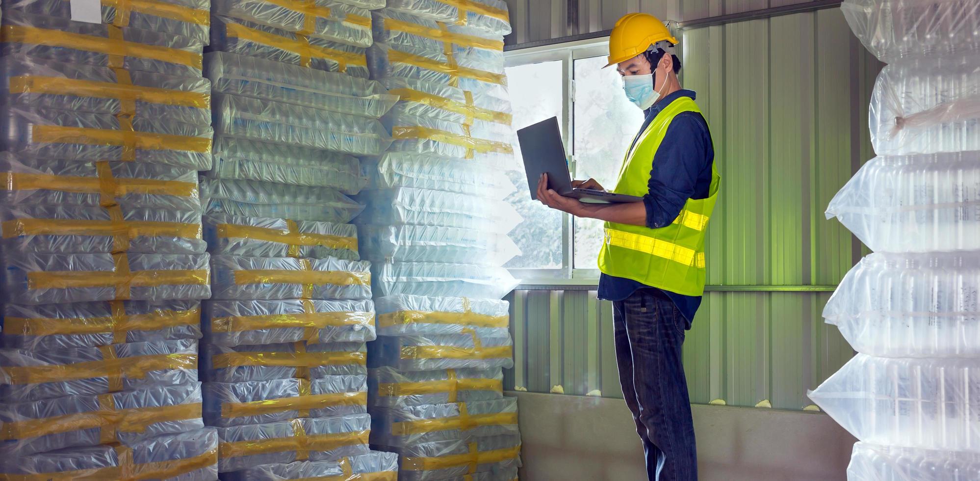 Young man worker and quality inspector in a factory checking number of white plastic bottles in the warehouse photo