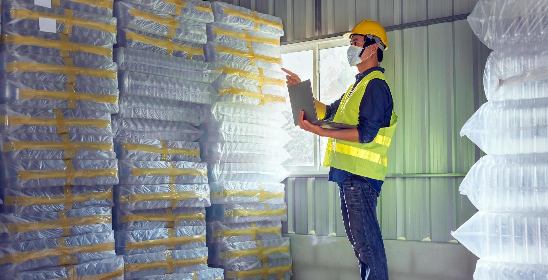 Young man worker and quality inspector in a factory checking number of white plastic bottles in the warehouse photo