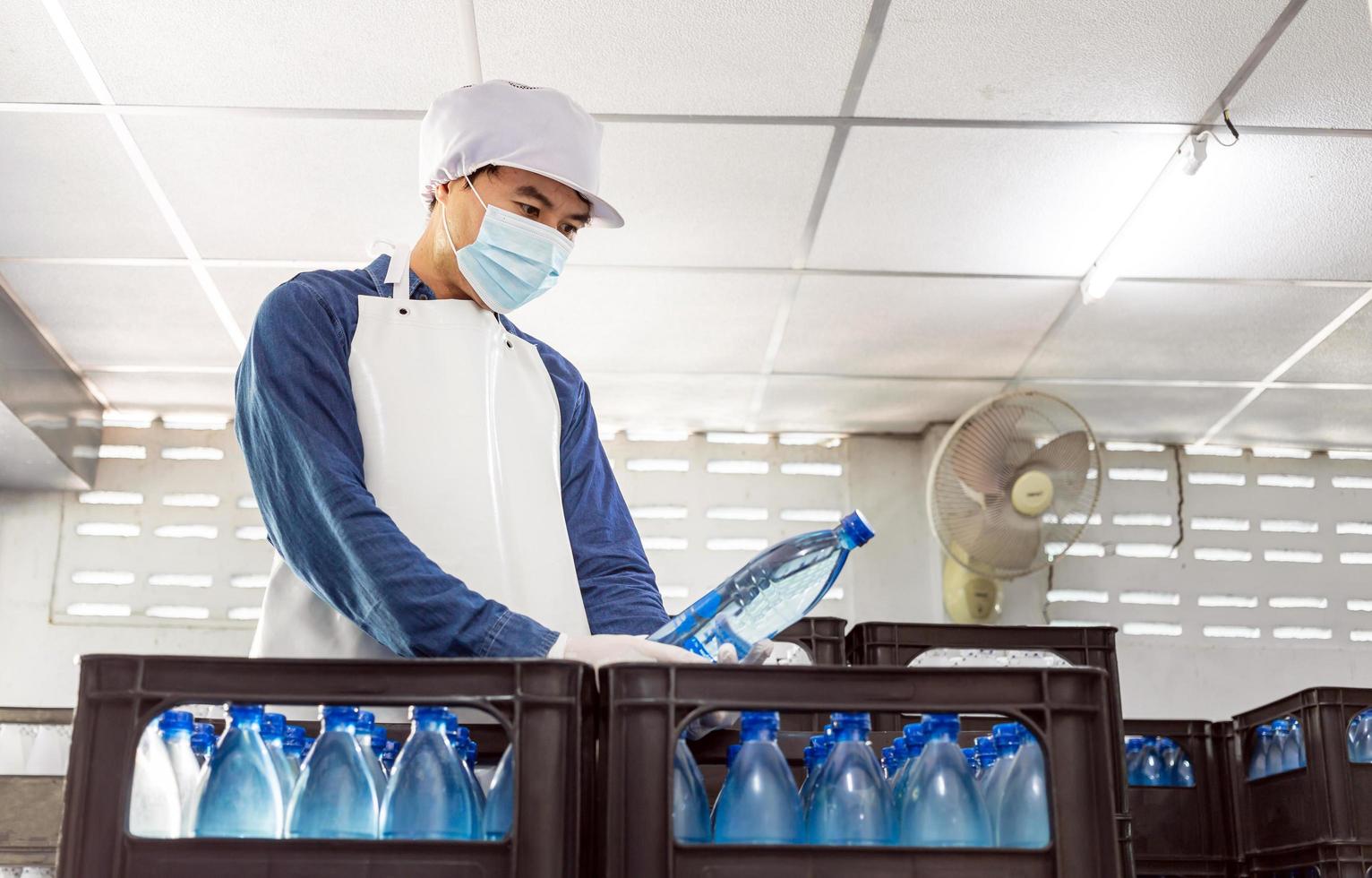 Young man worker or quality inspector in workwear and with a protective mask on his face working in checking bottled drinking water in drink water factory before shipment.drinking water business photo