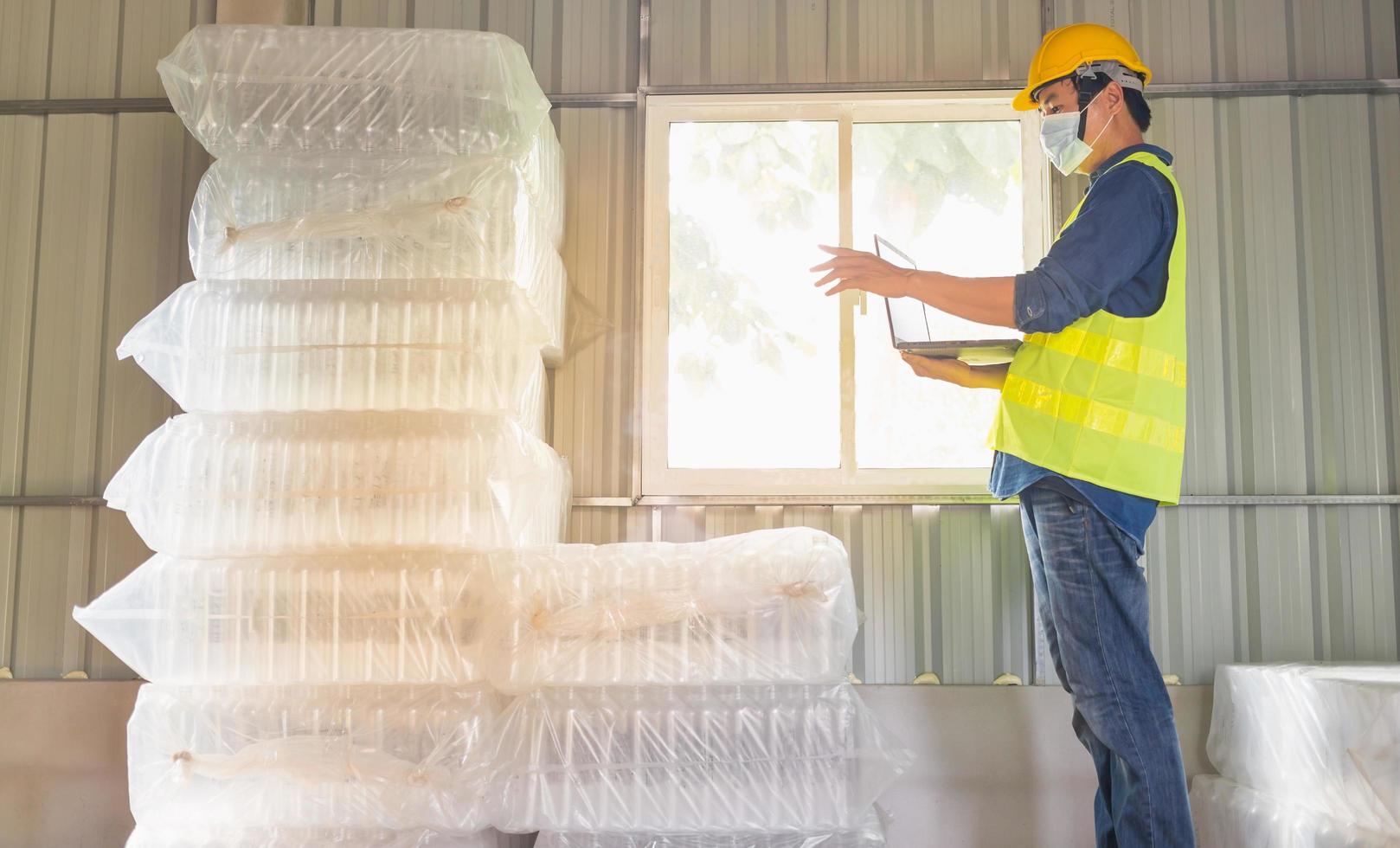 Young man worker and quality inspector in a factory checking number of white plastic bottles in the warehouse photo