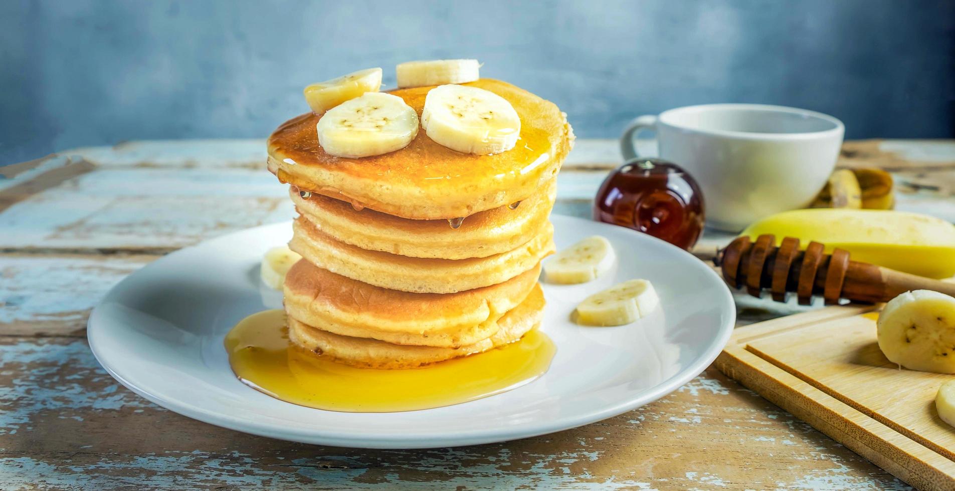 pila de panqueques de plátano con rodajas de plátanos frescos, una pila de panqueques caseros dulces con mantequilla y jarabe para el desayuno en un fondo de madera foto