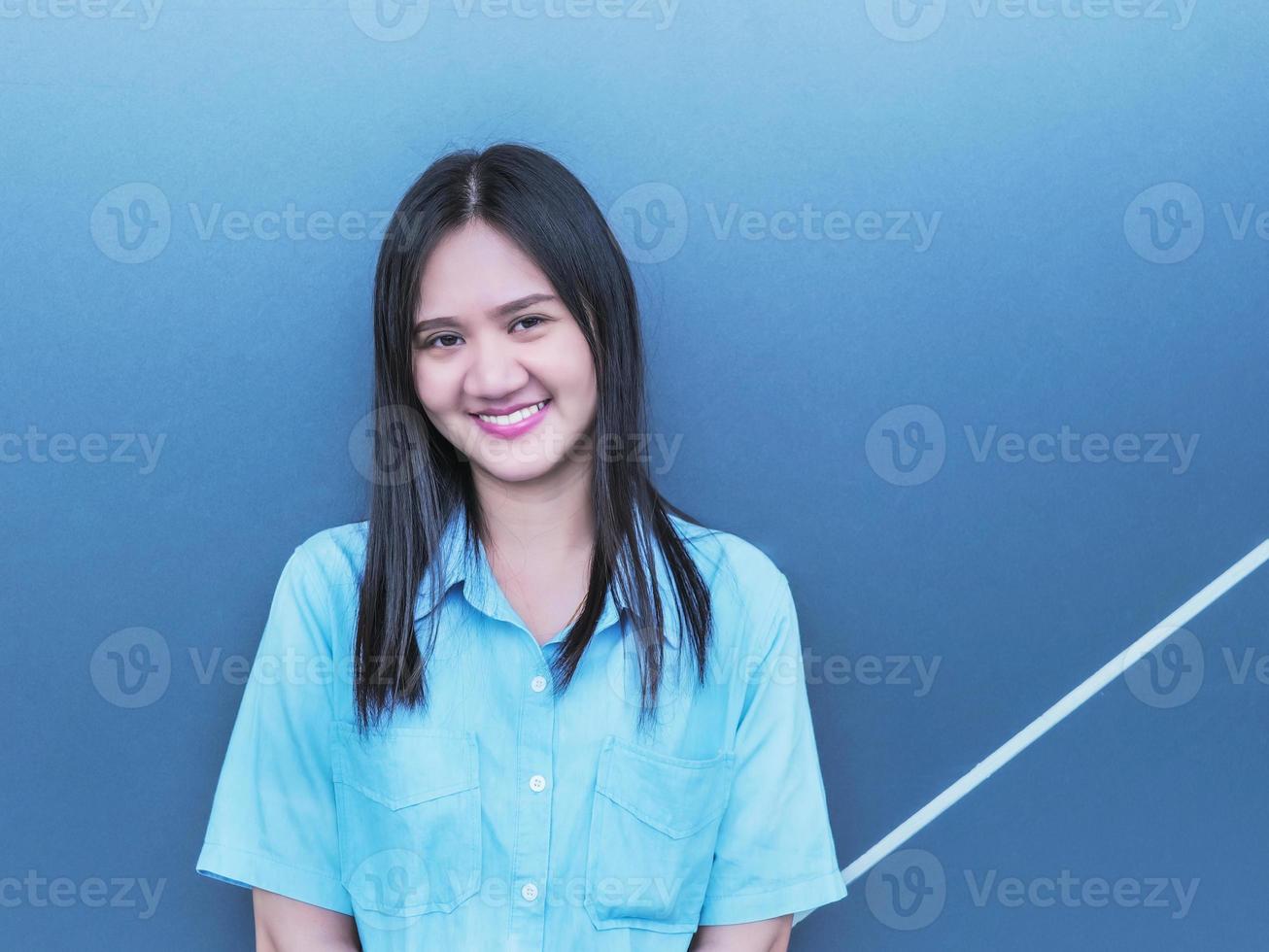 tomando un retrato de una mujer asiática con cabello negro y una camisa azul. con fondo negro foto