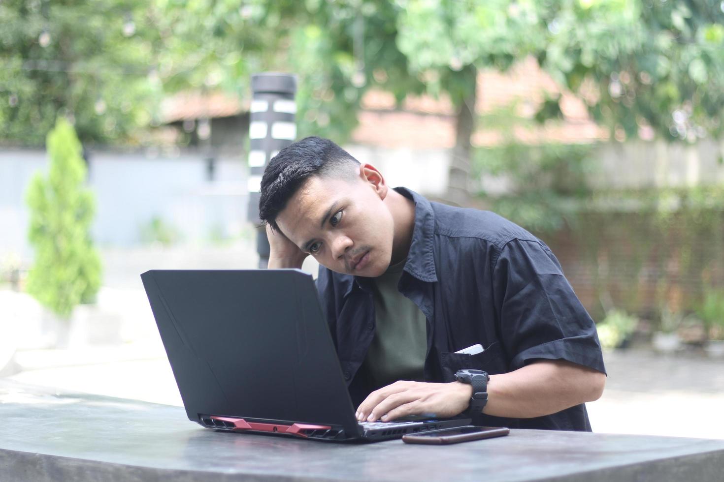 Attractive young Asian man using laptop confused in co-working space with unhappy face photo