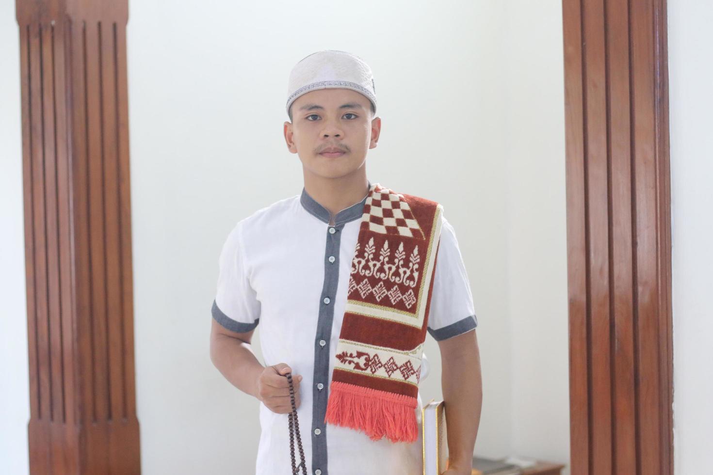 Young asian muslim praying in the mosque carrying a prayer mat photo