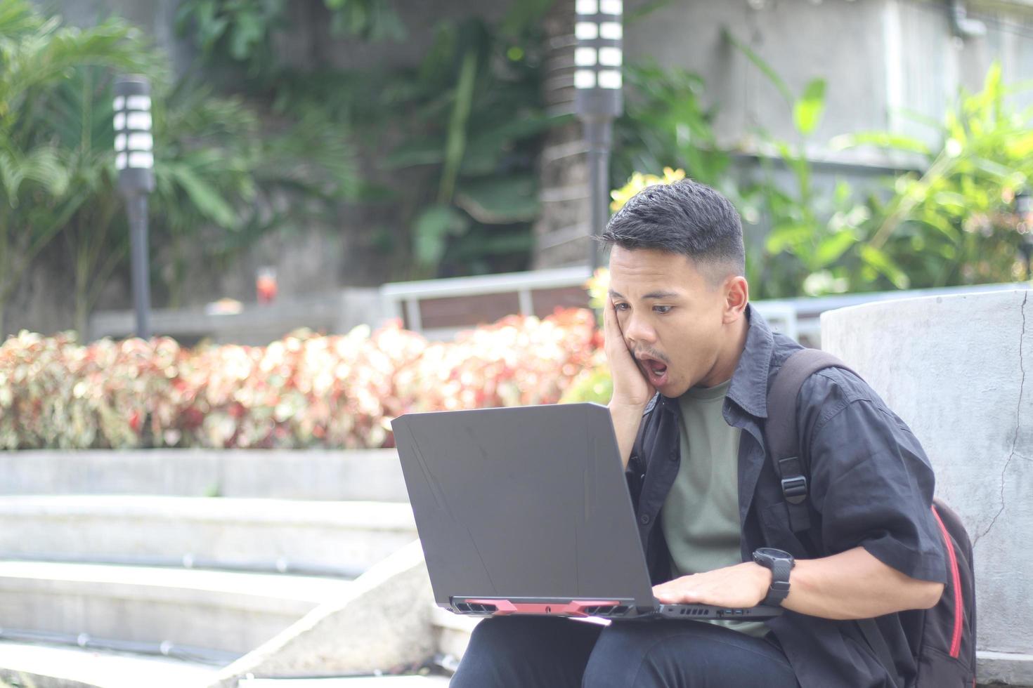 Attractive young Asian man using laptop confused in co-working space with unhappy face photo