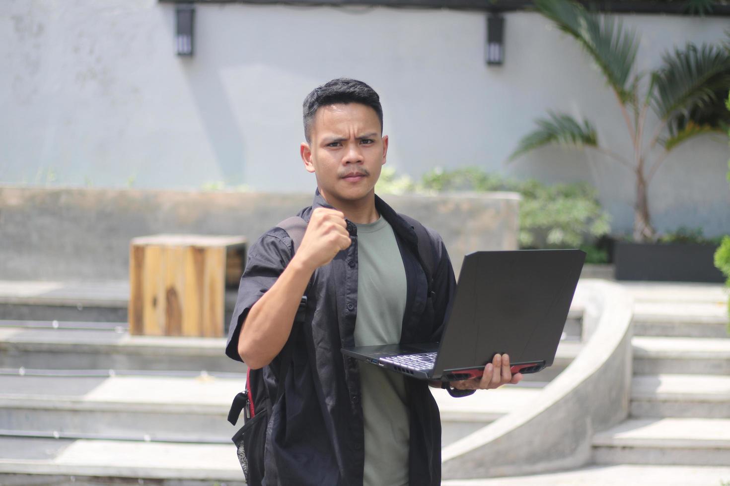 Attractive young Asian man using laptop in co-working space with happy face photo
