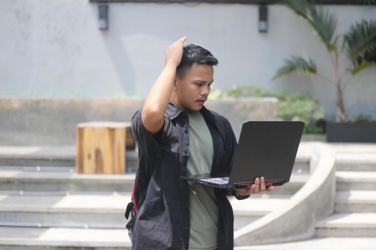 Attractive young Asian man using laptop confused in co-working space with unhappy face photo