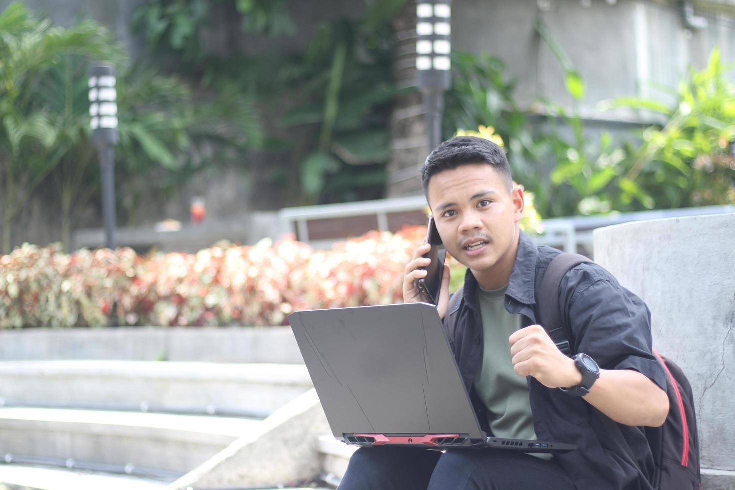 Attractive young Asian man using laptop in co-working space with happy face and calling her friend photo