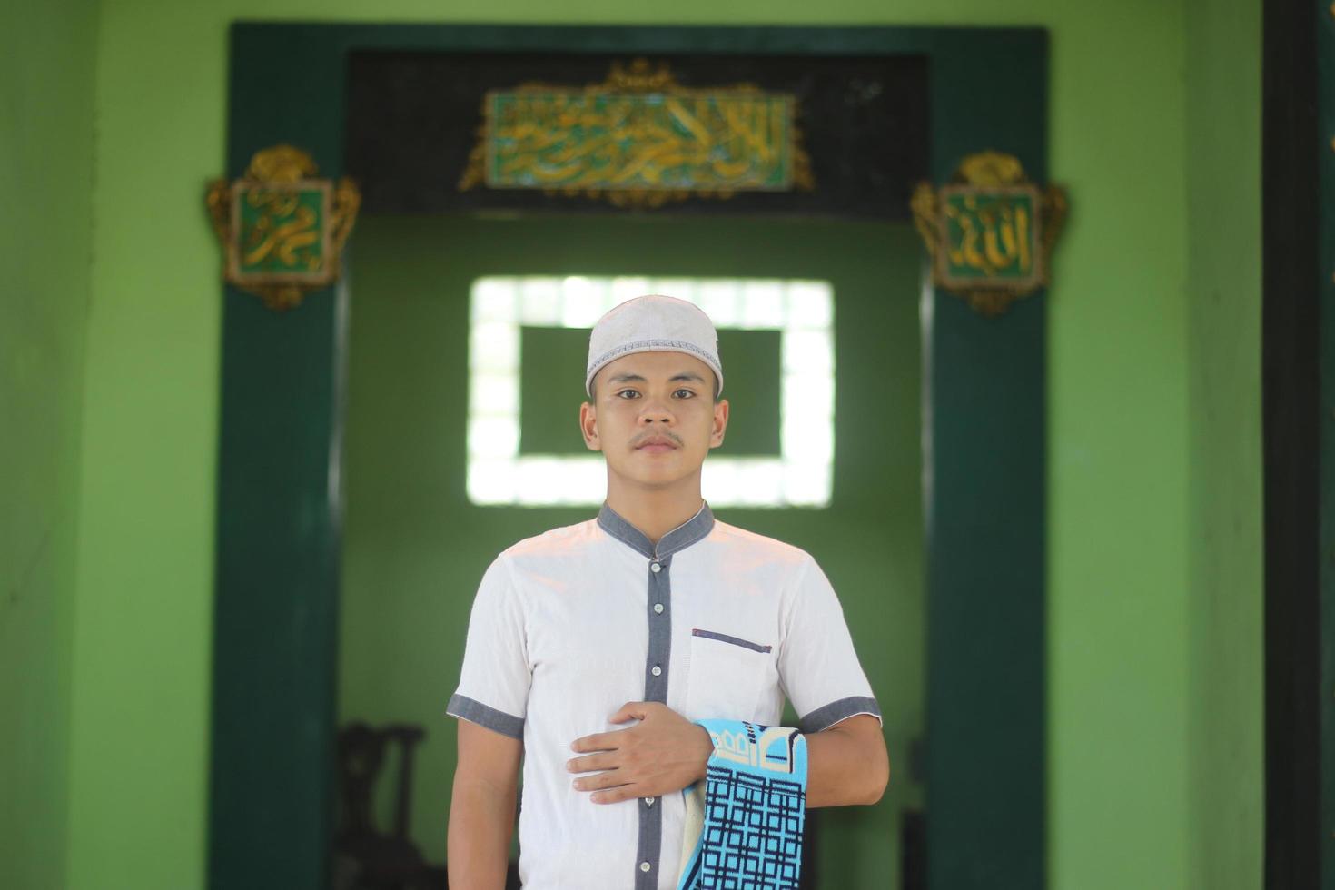 Young asian muslim praying in the mosque carrying a prayer mat photo