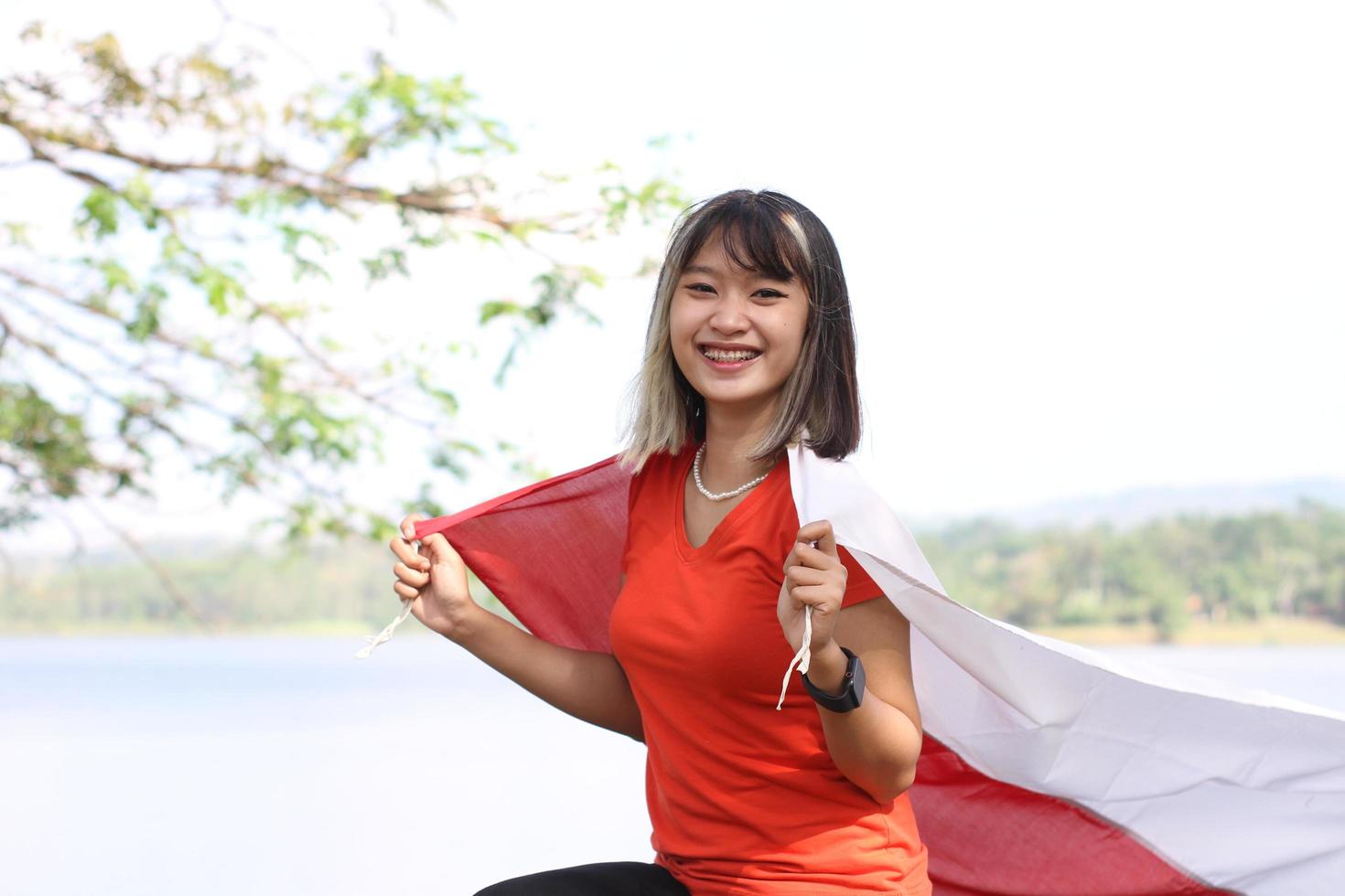 bella joven asiática que lleva la bandera indonesia con una cara alegre foto