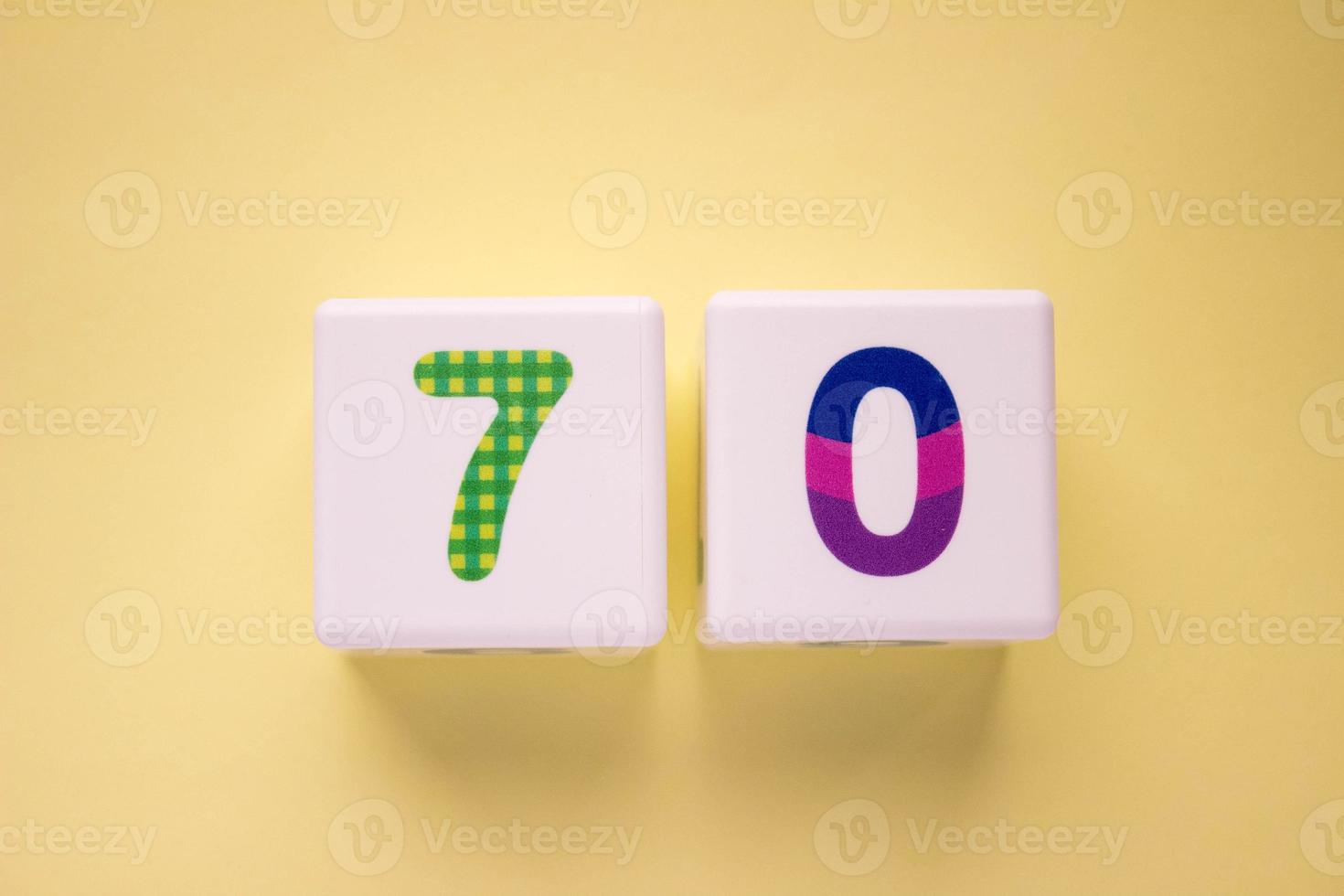 Close-up photo of a white plastic cubes with a colorful number 70 on a yellow background. Object in the center of the photo