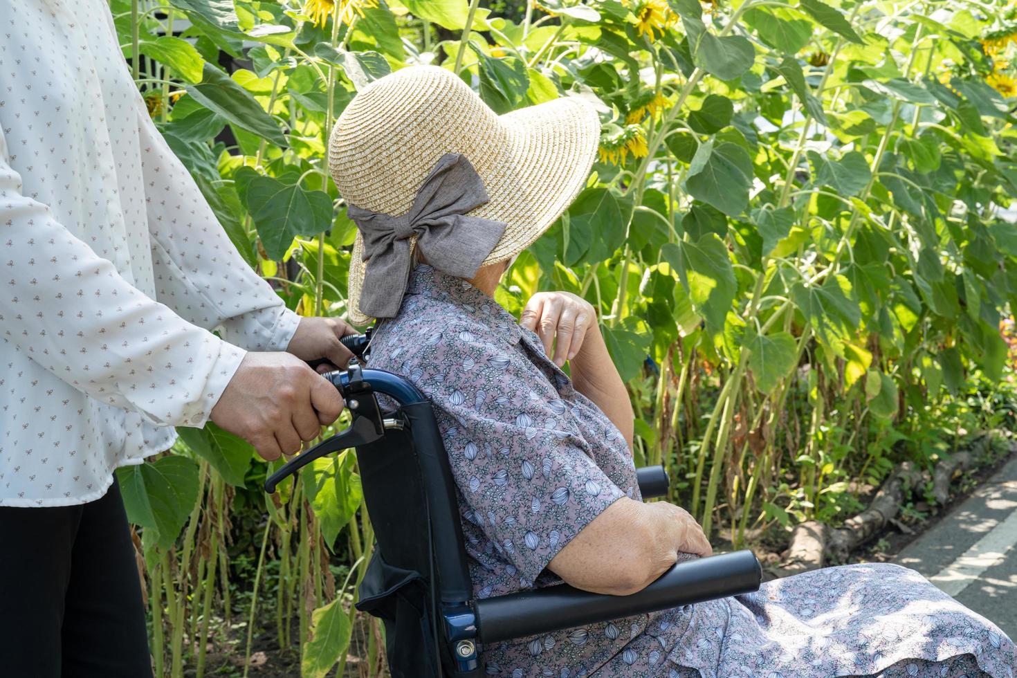 cuidador ayuda y cuida a una anciana asiática o anciana paciente sentada y feliz en silla de ruedas en el parque, concepto médico fuerte y saludable. foto