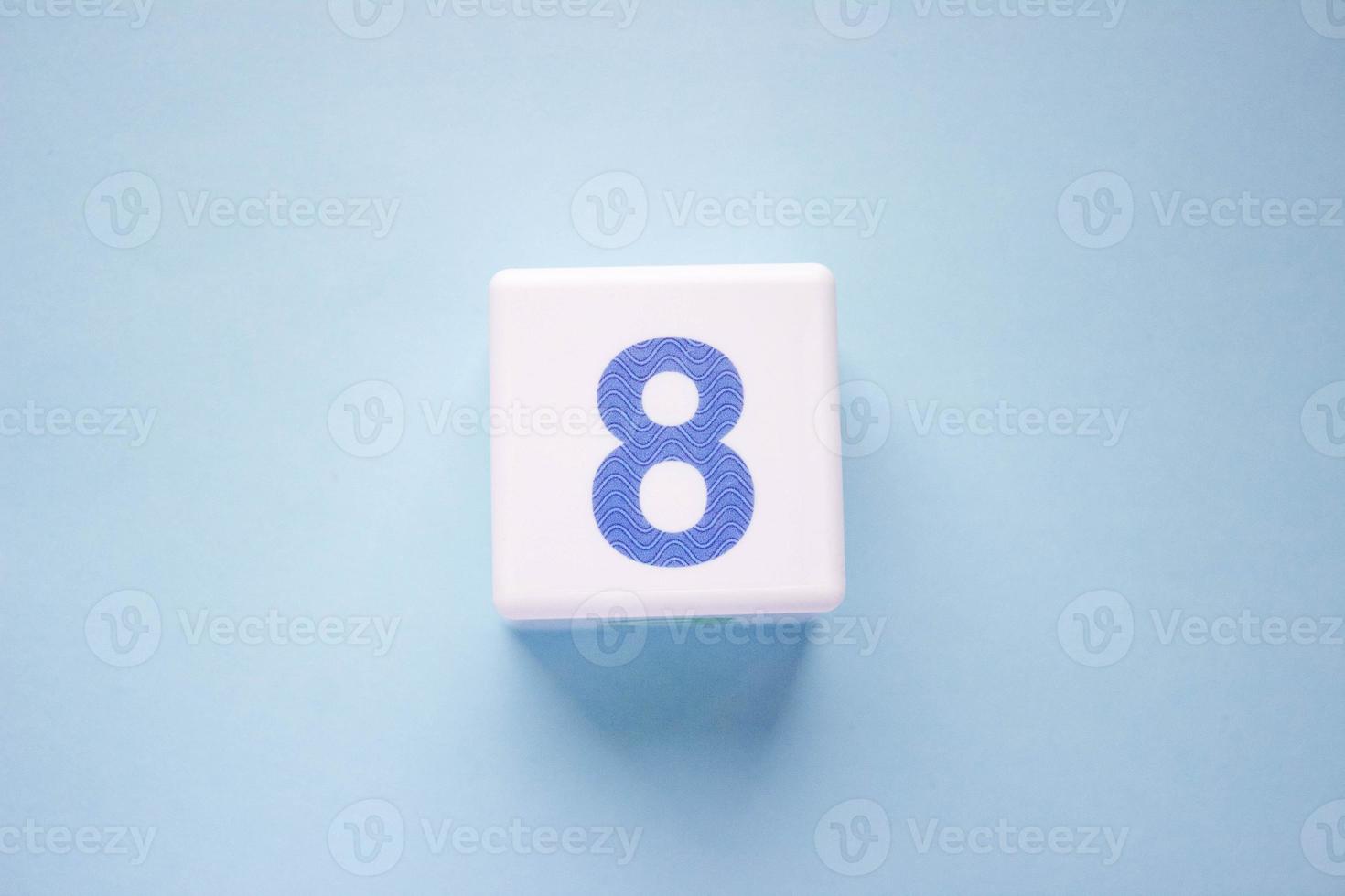 Close-up photo of a white plastic cube with a blue number 8 on a blue background. Object in the center of the photo