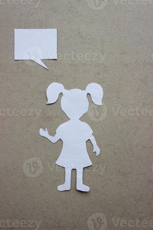 Silhouette of a girl in a dress and with ponytails made of white paper, cut by hand. On beige background photo