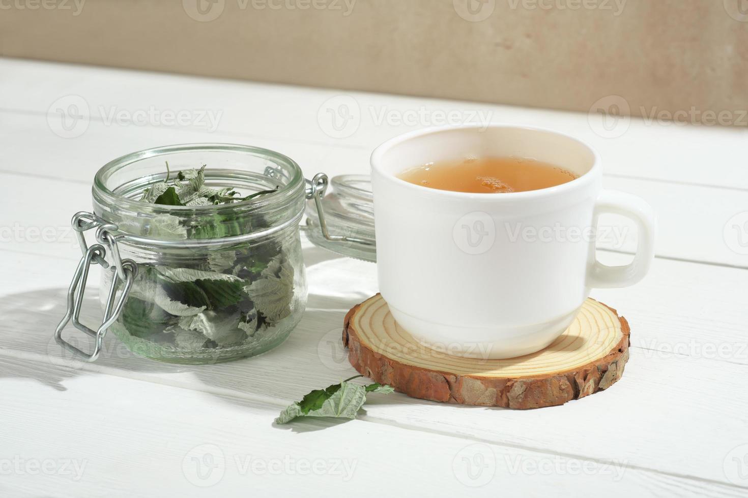 herbal tea in white cup with dry raspberry leaves in transparent glass jar. cold and flu natural healing tea. winter warming drinks with herbs photo