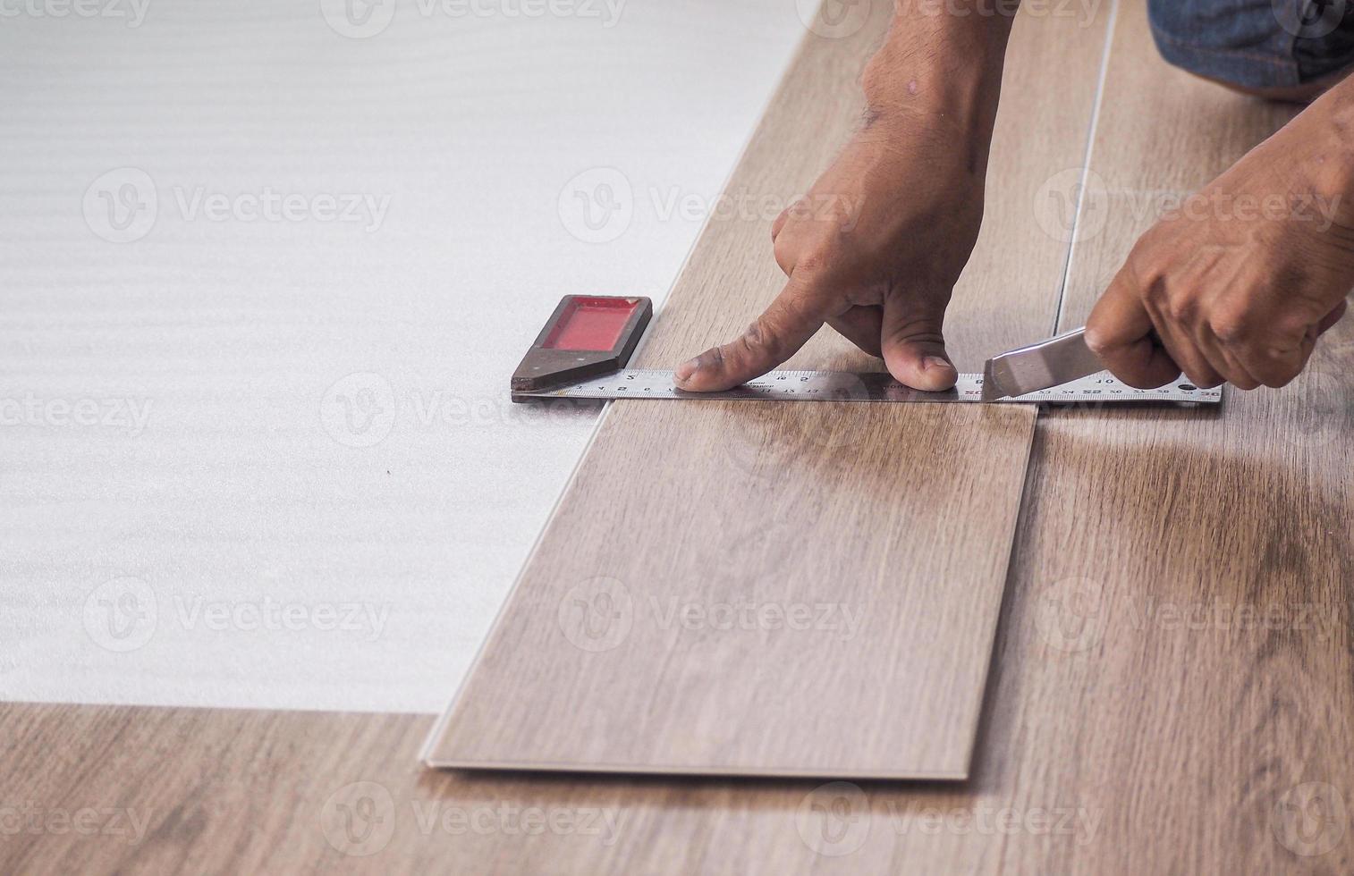 A technician is cutting luxury vinyl floor tiles with a cutter to lay the floor before placing it on the leveling foam. photo