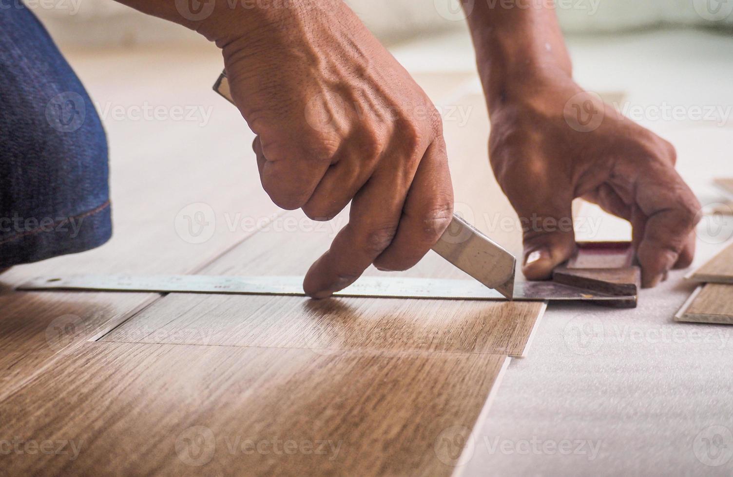 A technician is cutting luxury vinyl floor tiles with a cutter to lay the floor before placing it on the leveling foam. photo