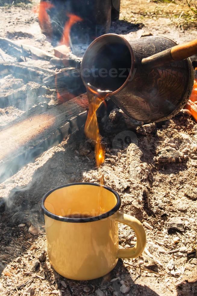 Yellow metal cup with hot coffee and cezve on the background of bonfire. photo