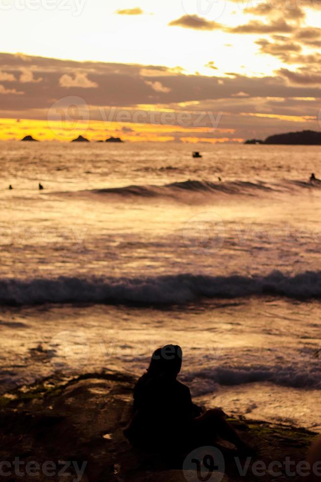 río de janeiro, rj, brasil, 2022 - personas en silueta miran la puesta de sol en arpoador rock, playa de ipanema foto