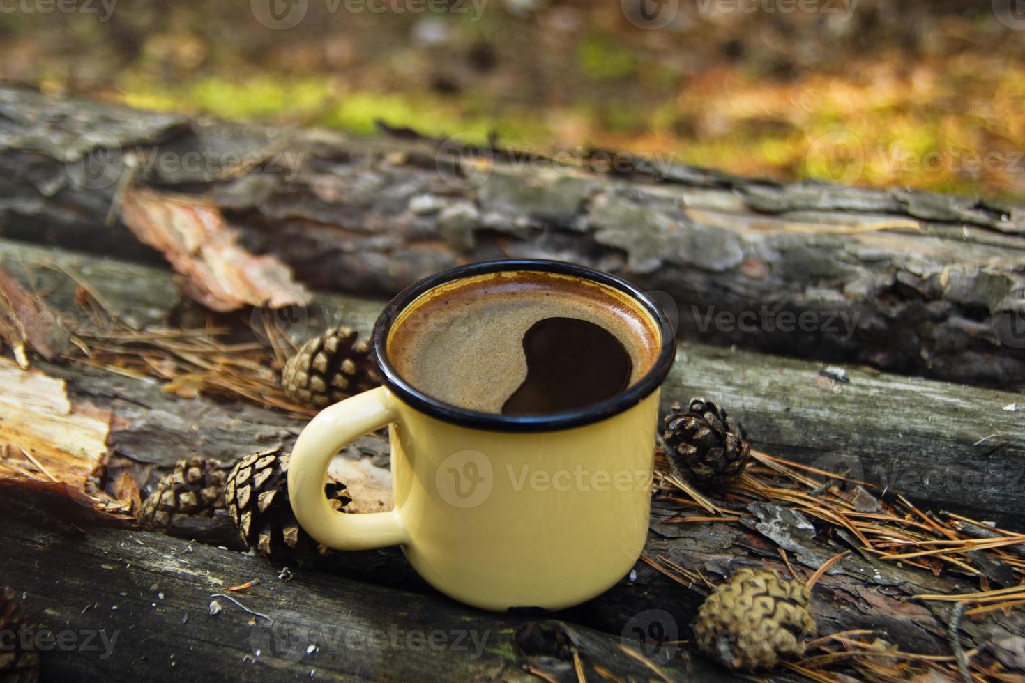 Yellow metal  cup with hot coffee on the wooden background with the coins, needles and bark of tree. photo