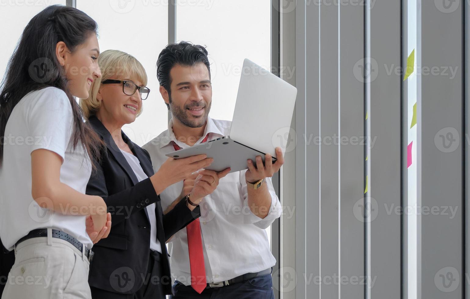 Happy diversity business people stands using laptop computer together for remote working at the office window. photo