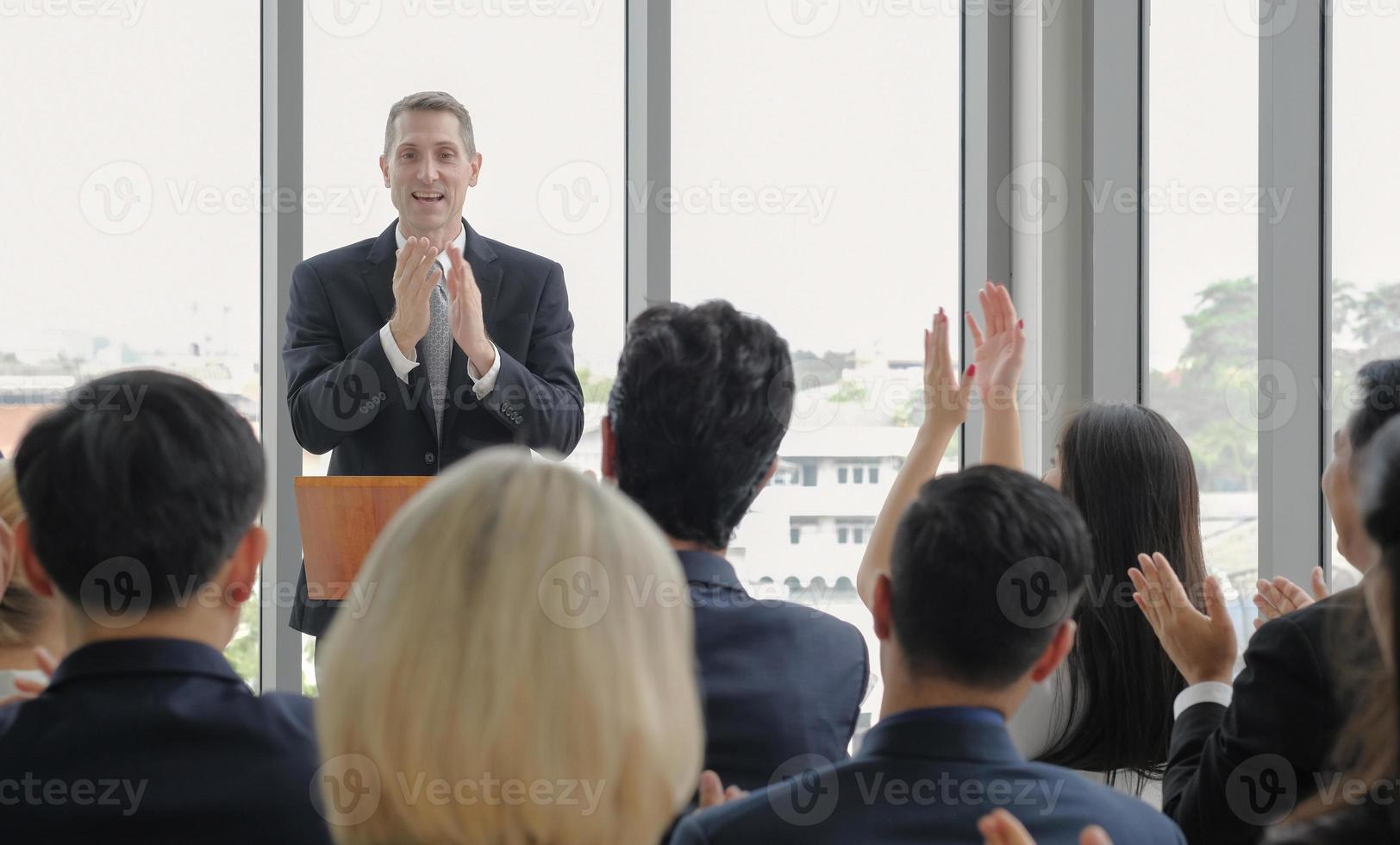 Senior male public speaker applauding together with audience in corporate seminar event at conference room. photo