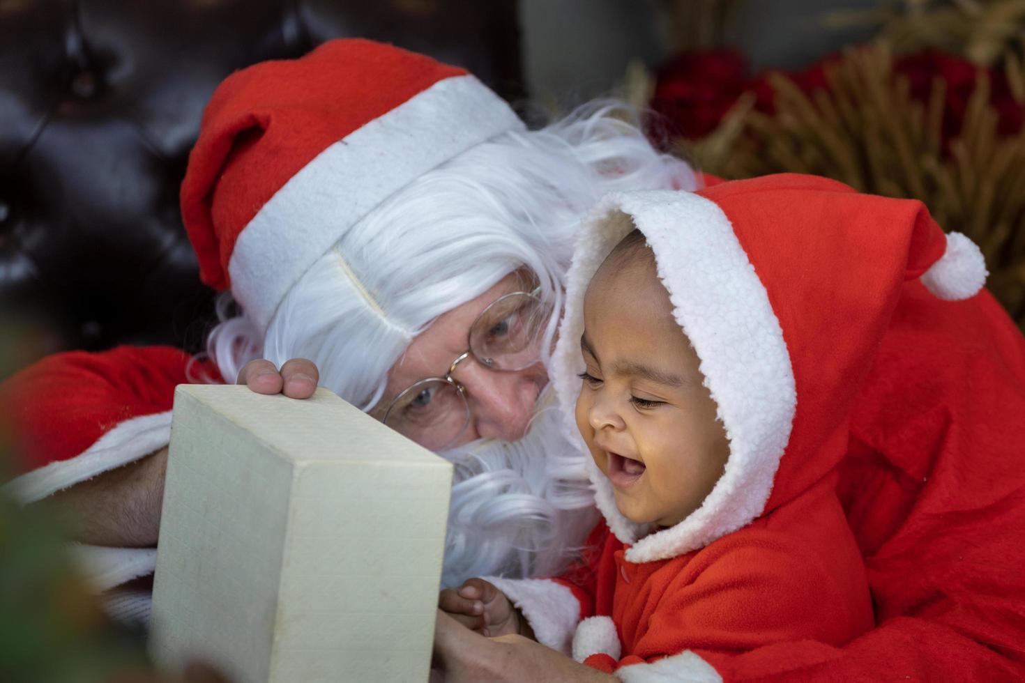 African American baby is opening christmas present with Santa claus at night for season celebration photo