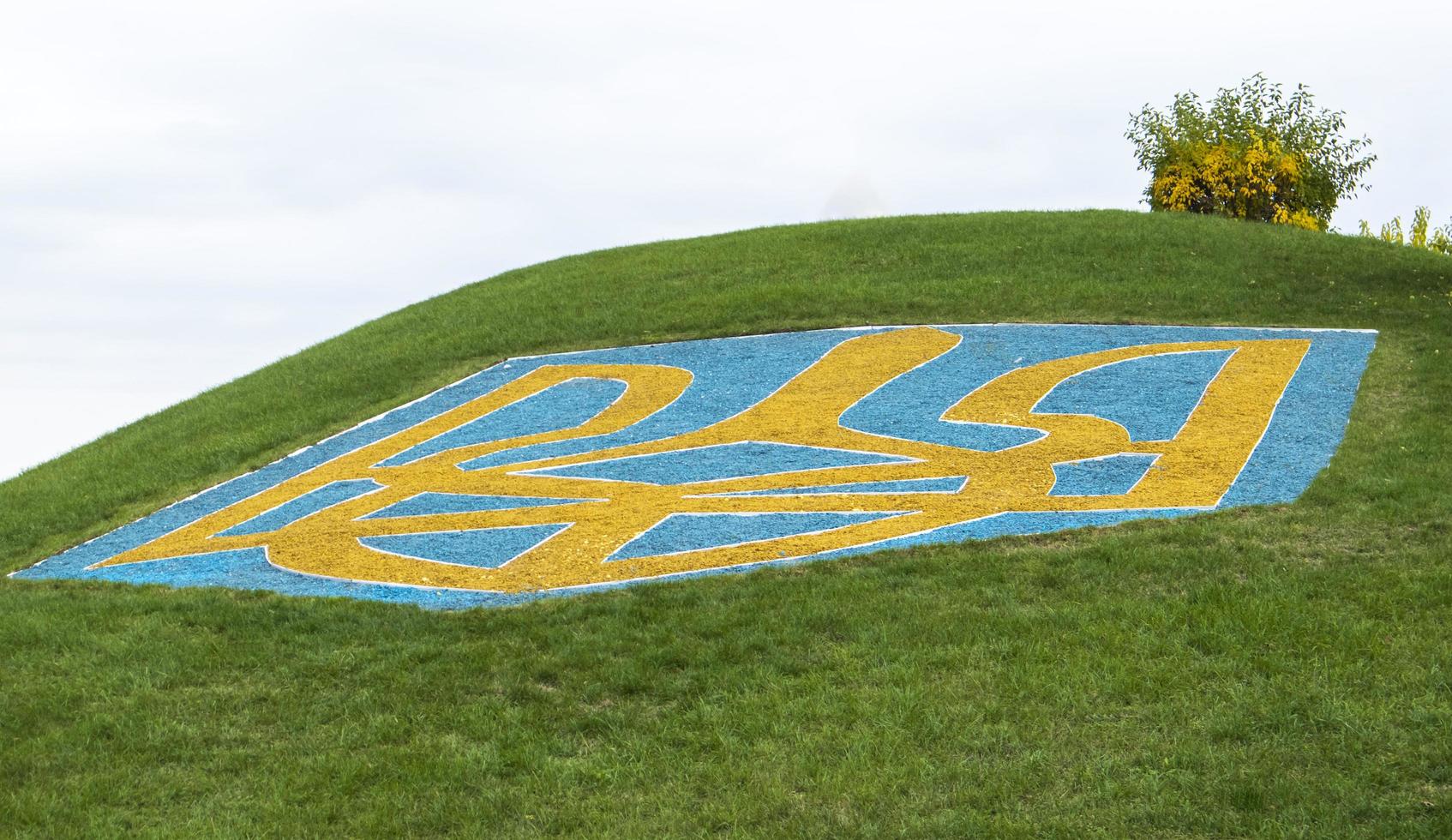 el gran escudo de armas de ucrania sobre un césped verde bordeado de piedras azules y amarillas contra un cielo azul. el símbolo oficial del estado. tridente del principe vladimir. ucrania, Kyiv - 08 de octubre de 2022. foto