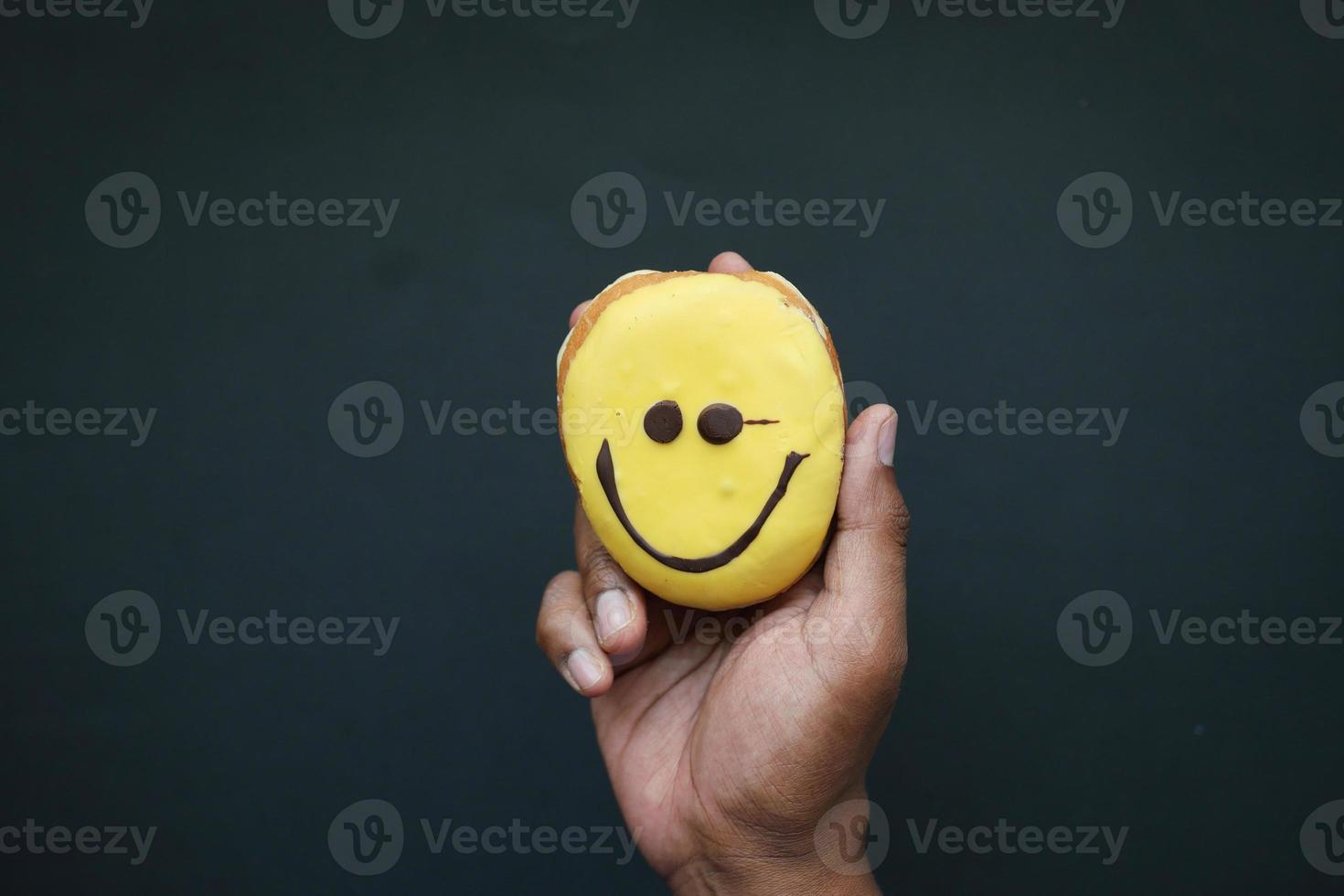 holding a smile face design donuts against black background photo