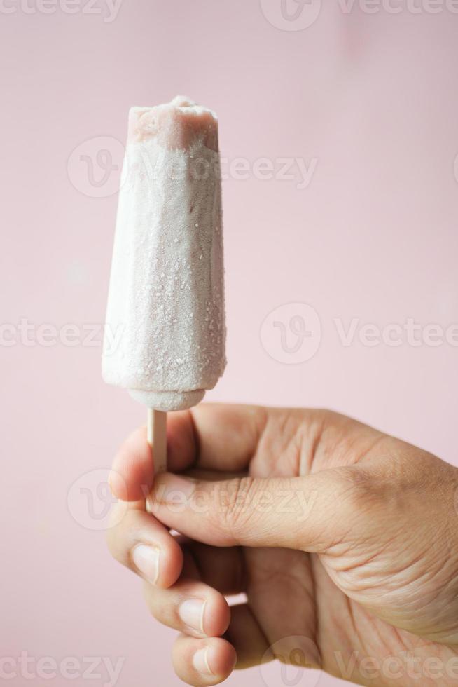 person hand holding ice cream against blue background with copy space photo