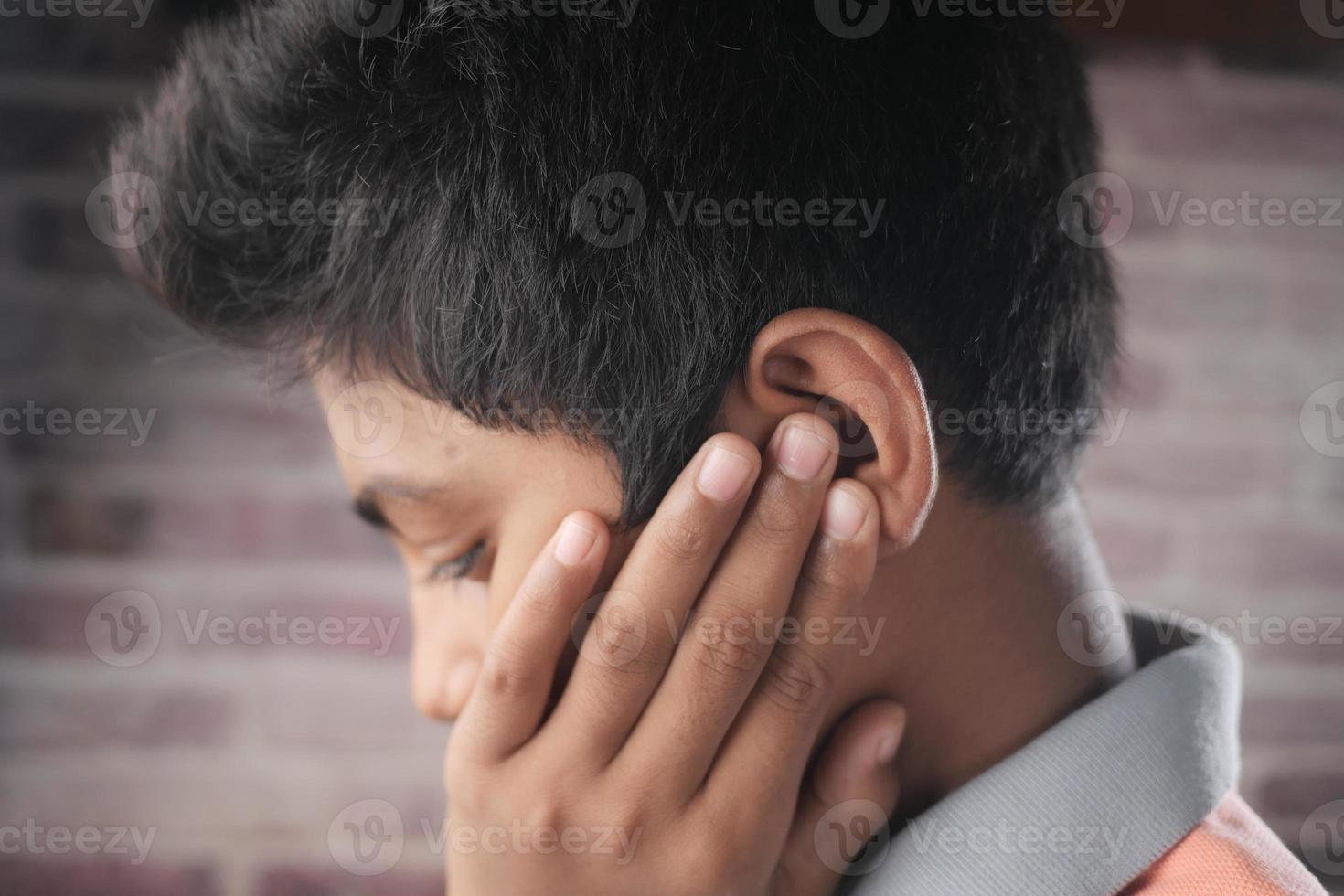 teenage boy having ear pain touching his painful ear , photo