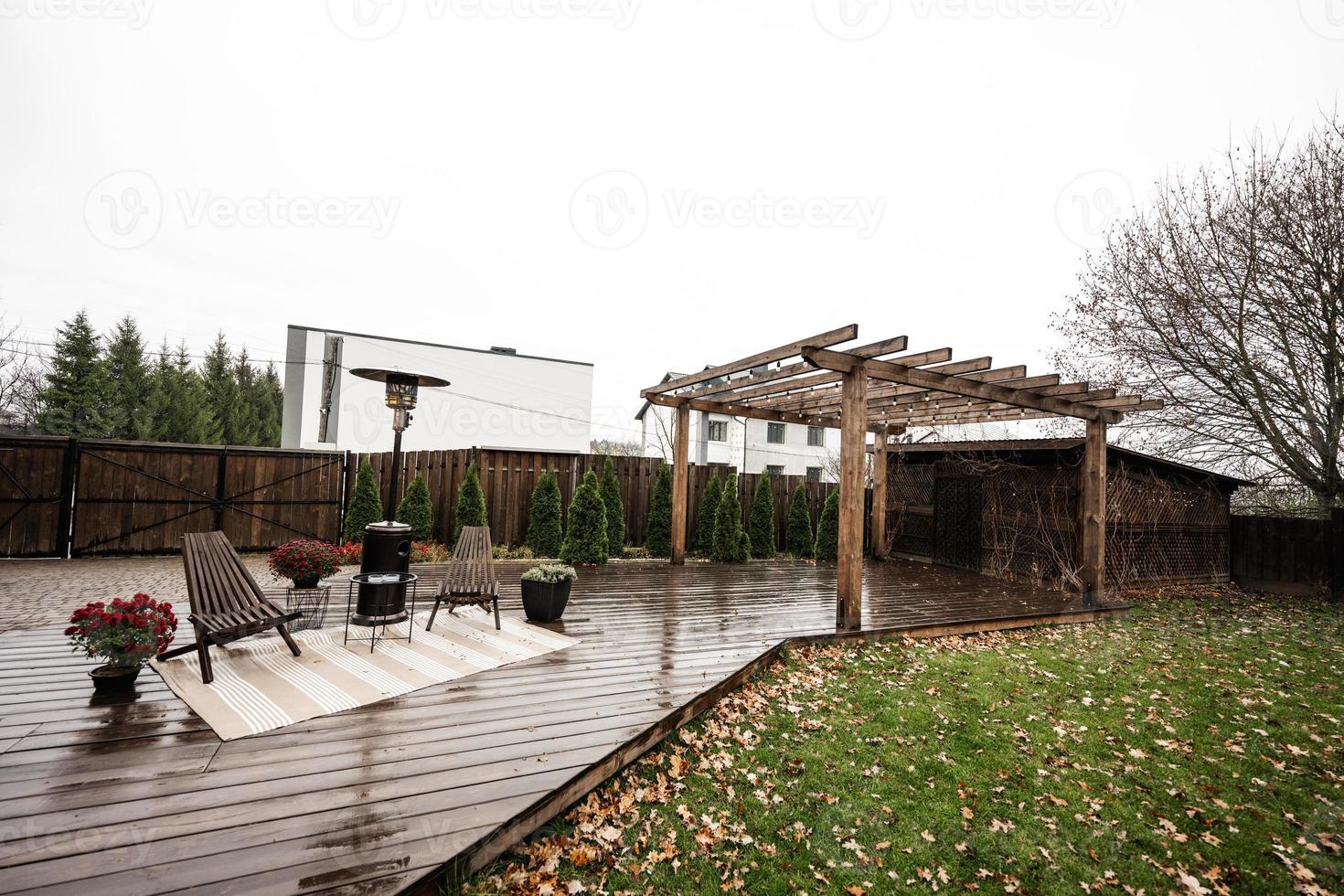 Stainless steel metal gas outdoor patio heater with wooden chairs and pot with flowers at wet terrace. Place to relax. photo