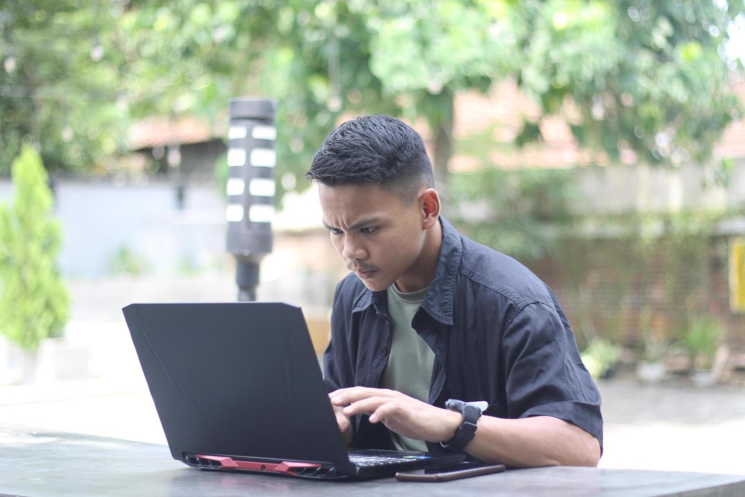 Attractive young Asian man using laptop confused in co-working space with unhappy face photo