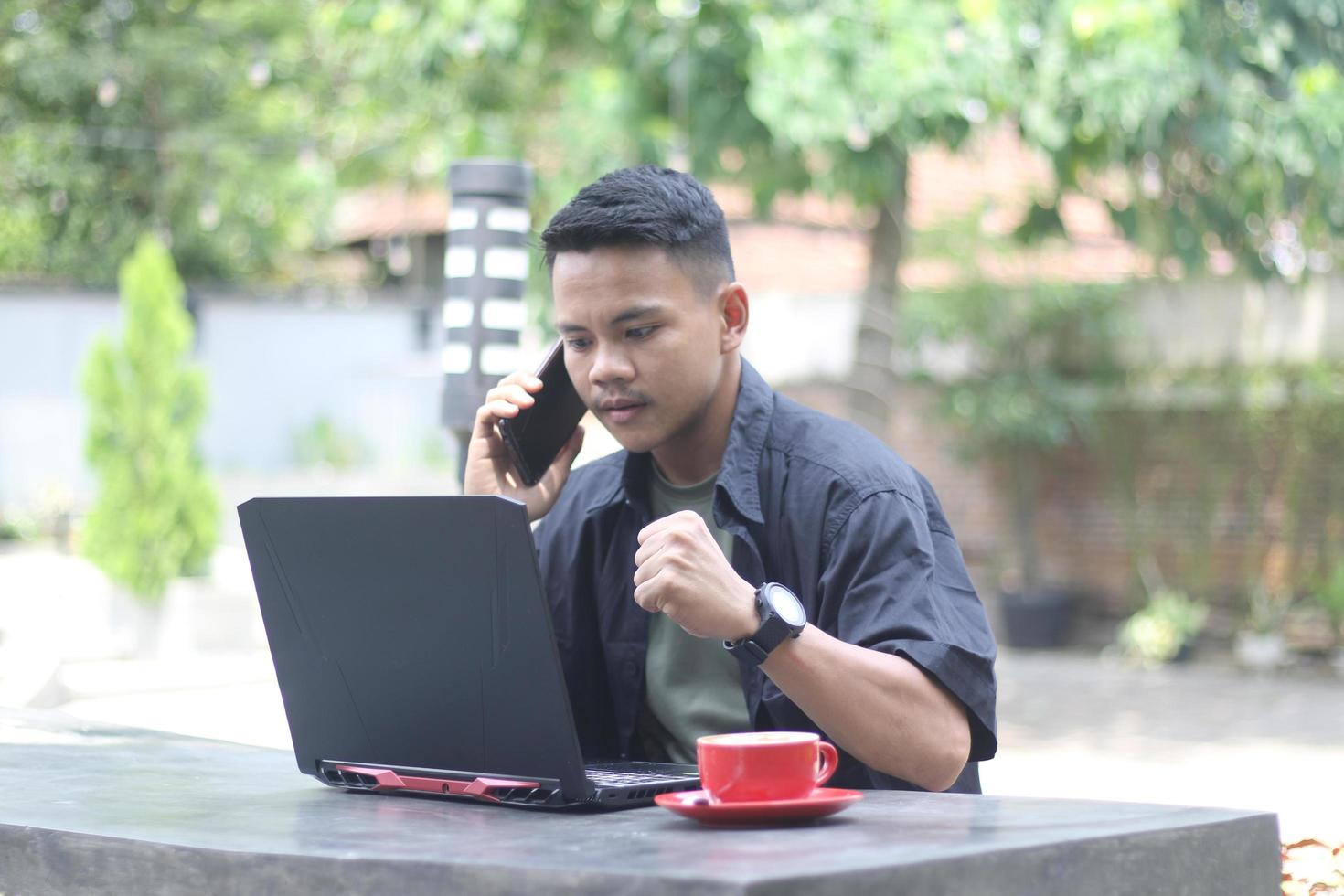 Attractive young Asian man using laptop in co-working space with happy face and calling her friend photo