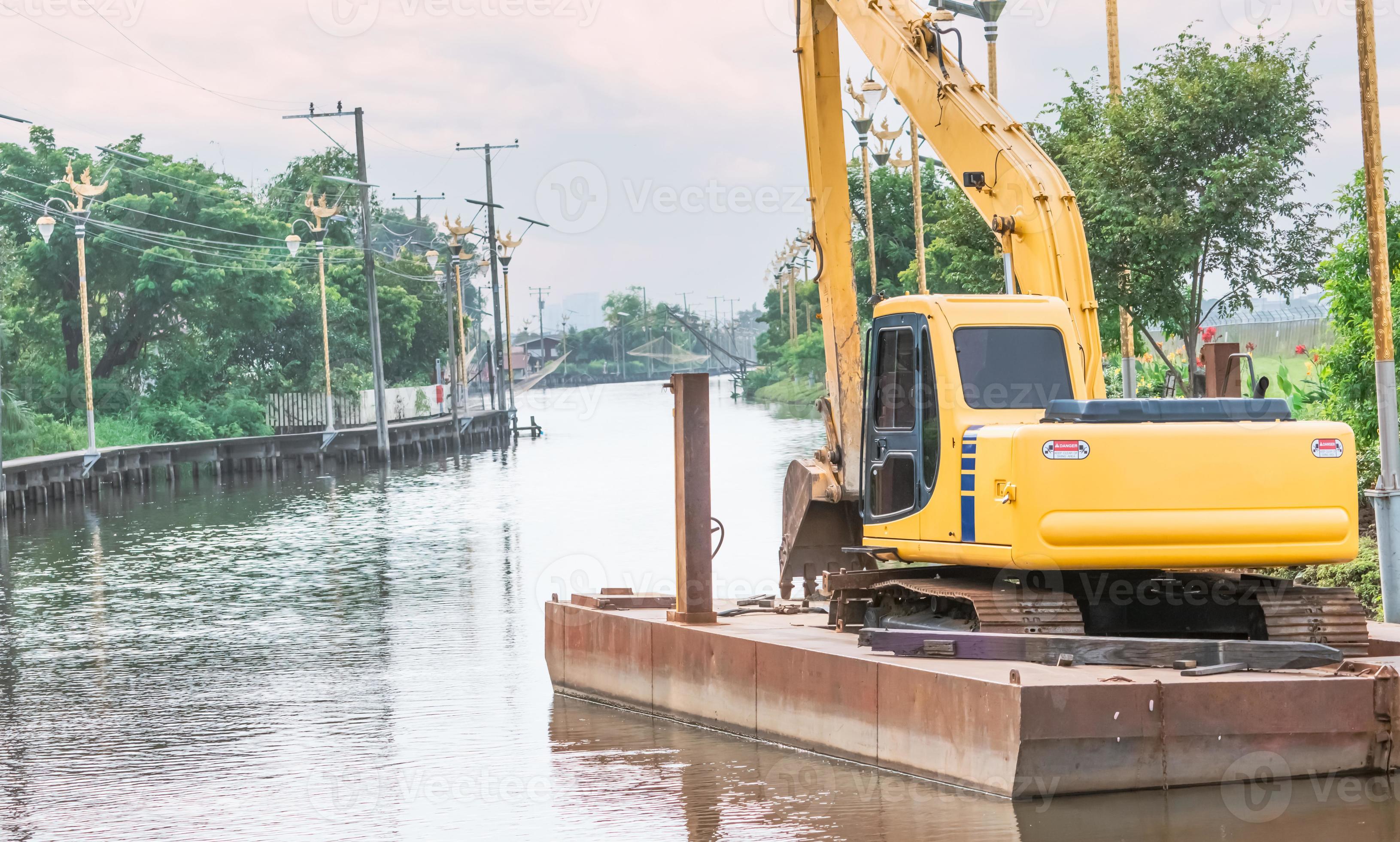 A yellow backhoe parked on a raft after dredging a canal. Backhoe on a
