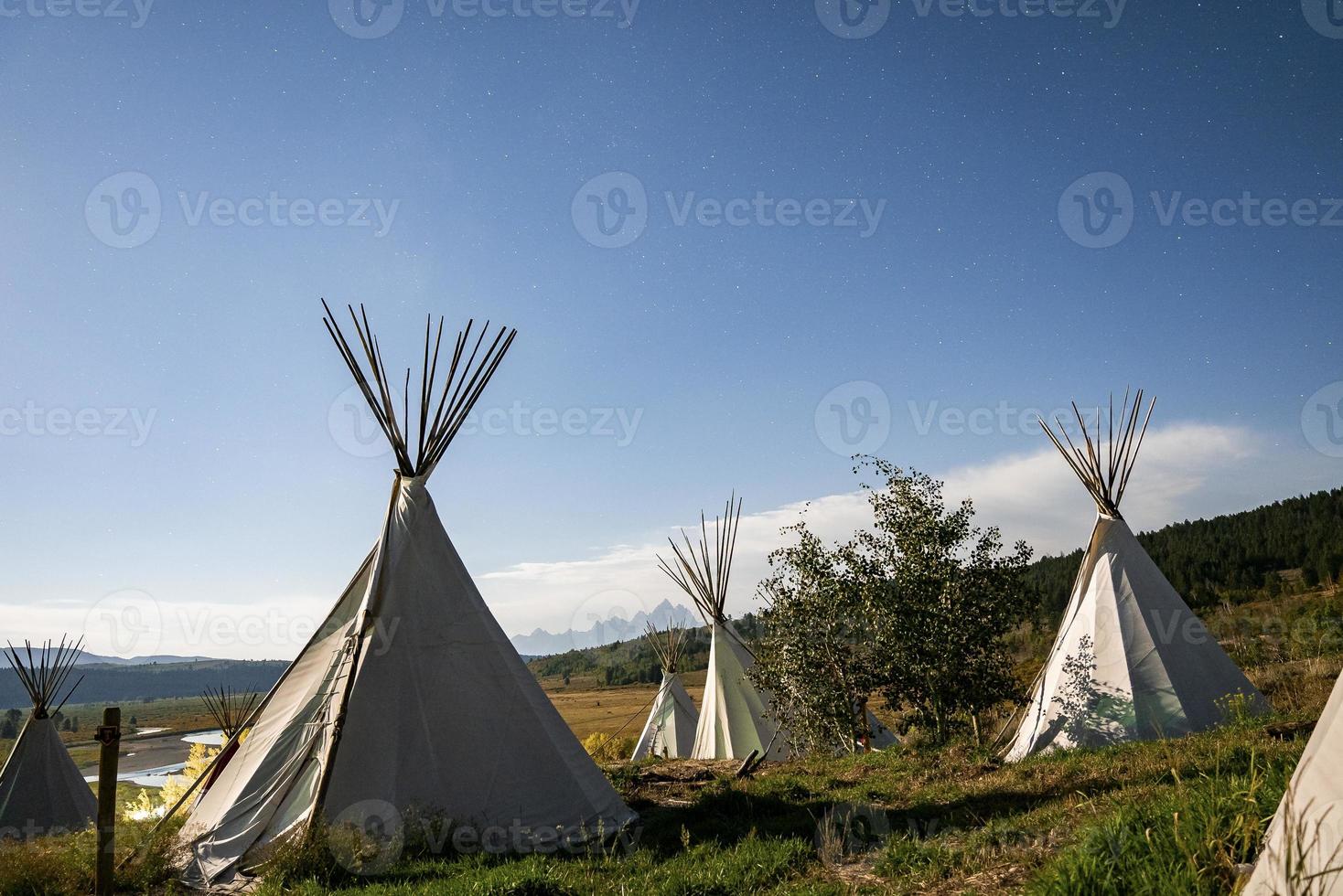 View of teepees on grassy field with blue sky in background during summer photo