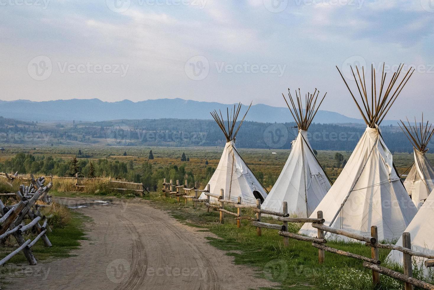 Dirtroad amidst teepees on field with cloudy sky in background at Yellowstone photo