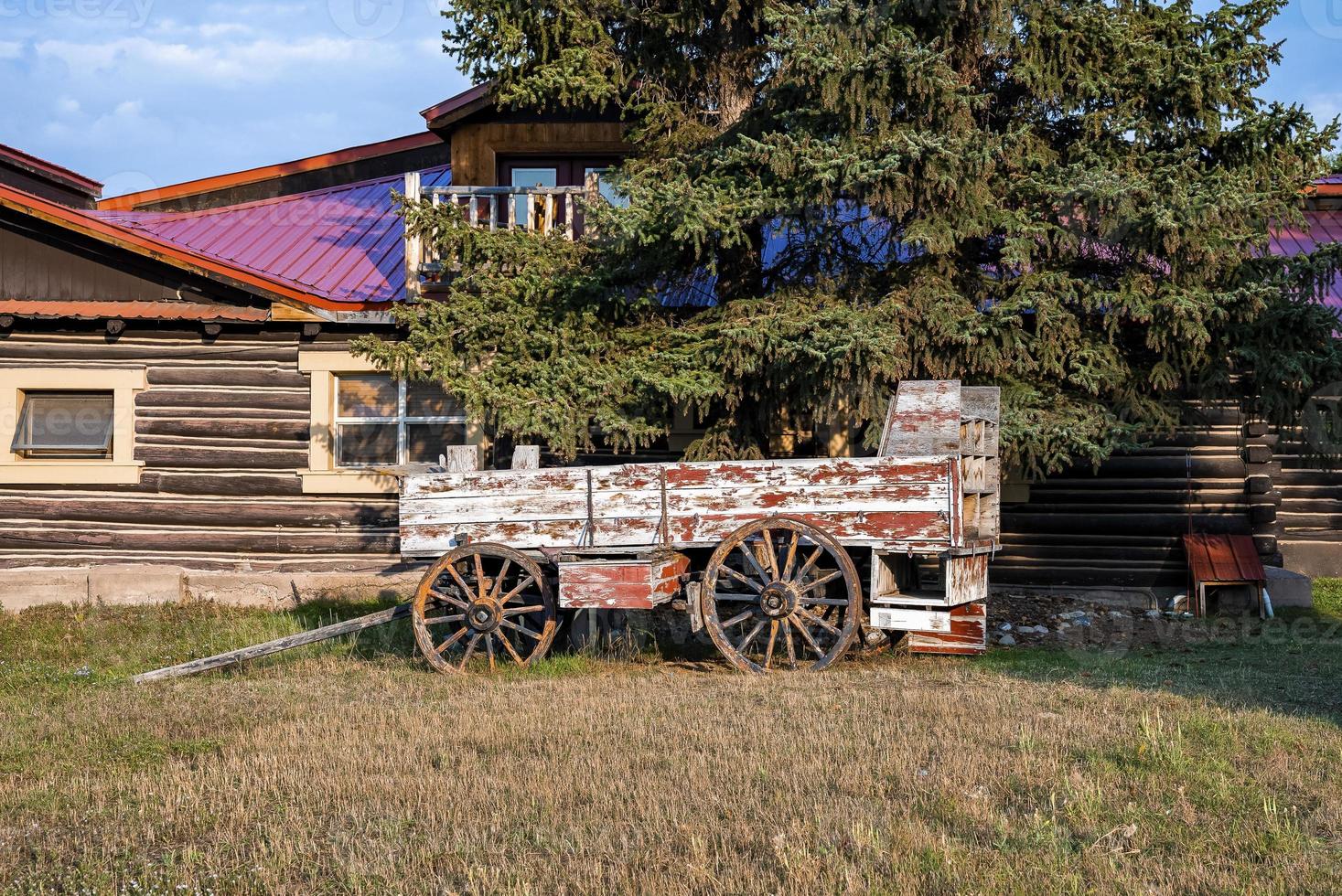 Old obsolete wagon under tree against log cabin during sunny day photo