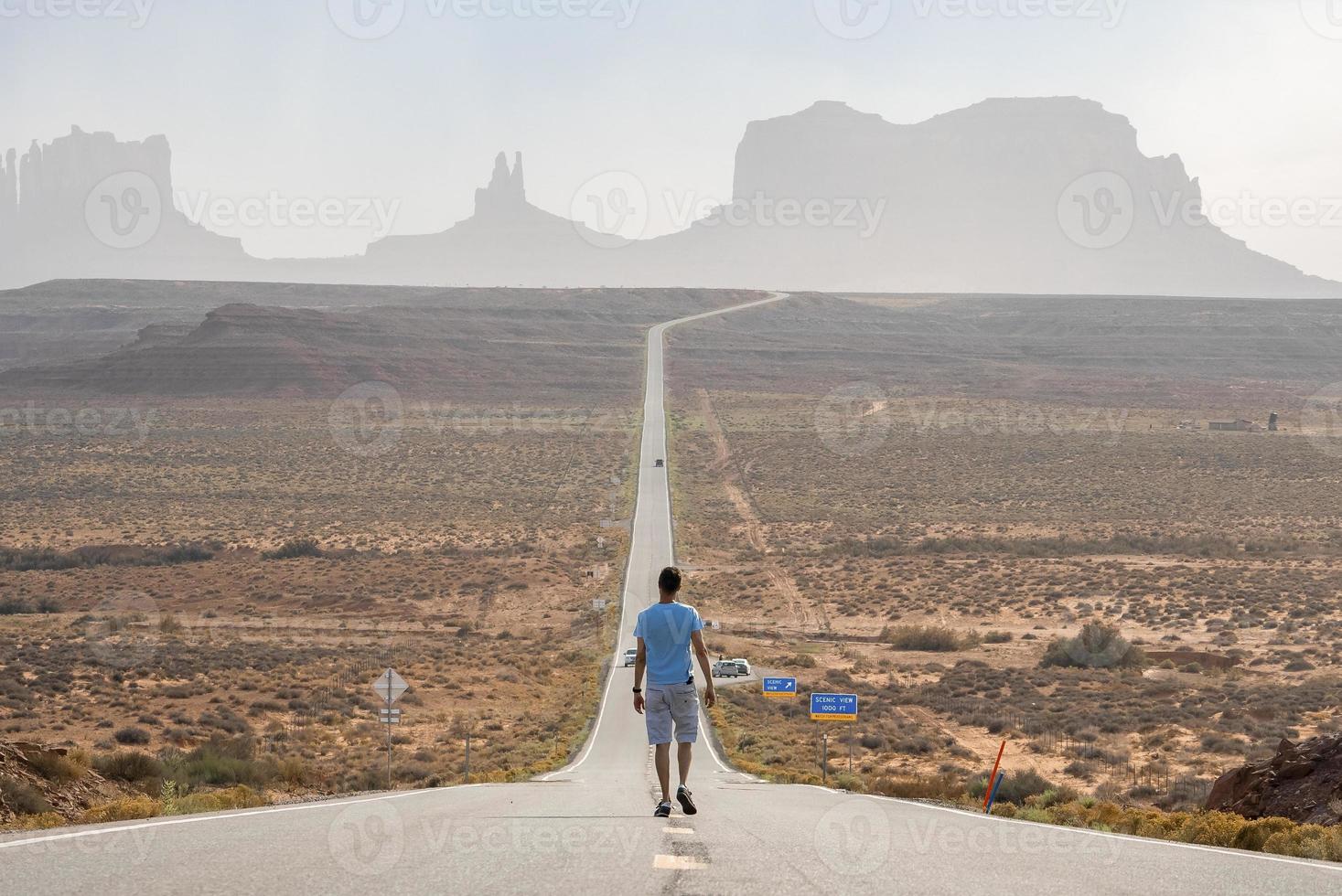 Traveler walking on road amidst landscape leading towards Monument valley photo