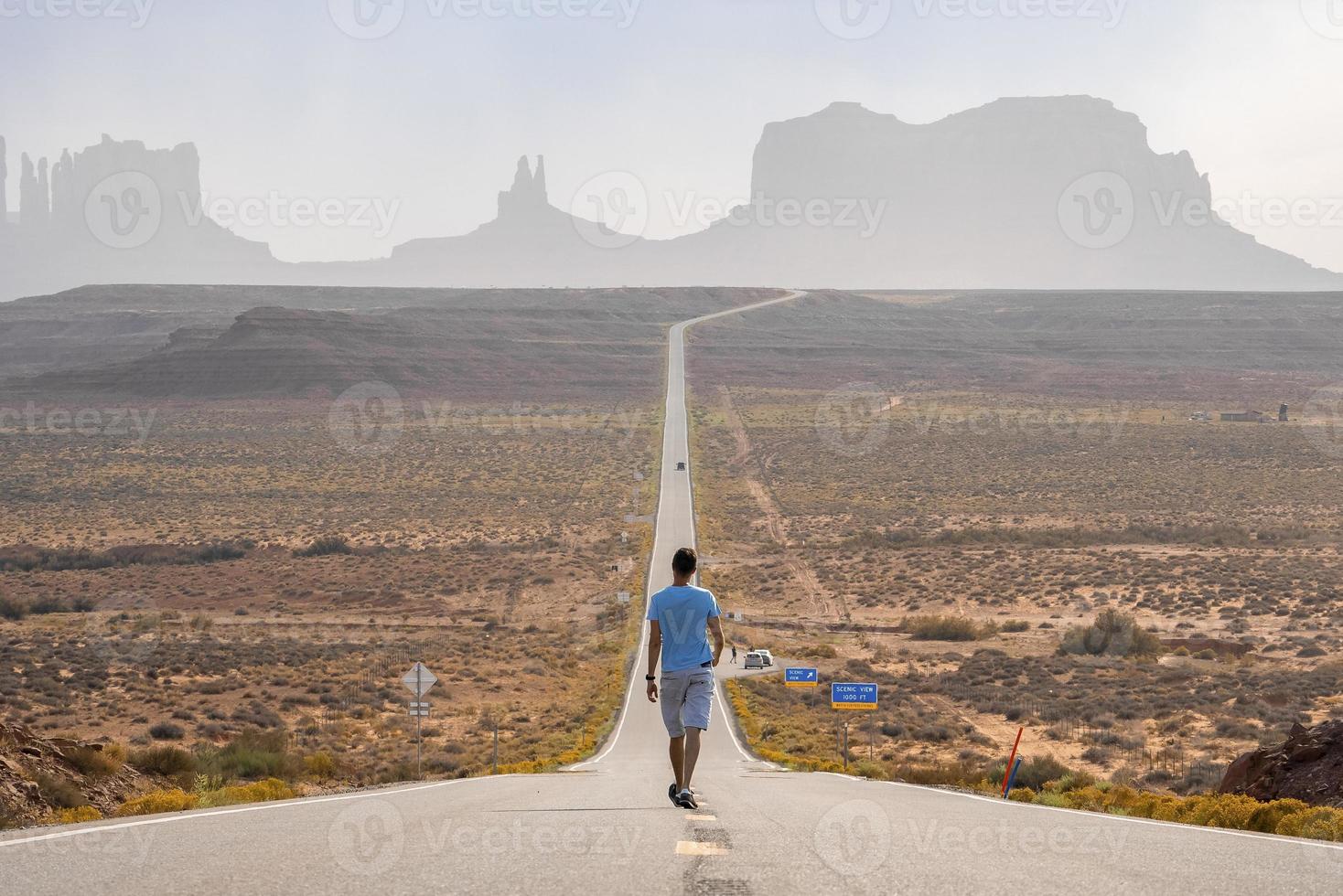 Male tourist walking on road leading towards Monument valley during summer photo