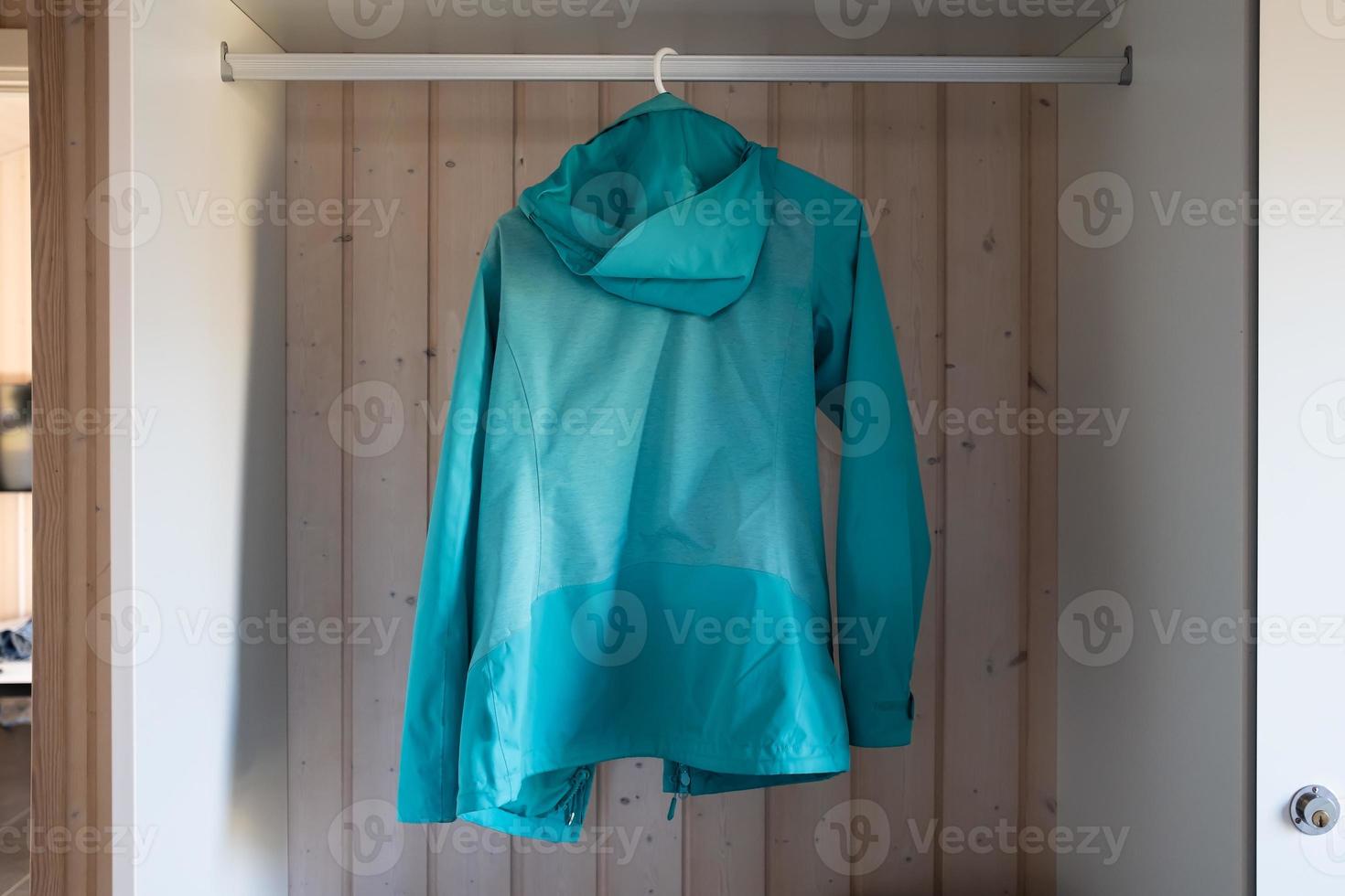 Blue windbreaker with a hood on a hanger in an open closet. photo