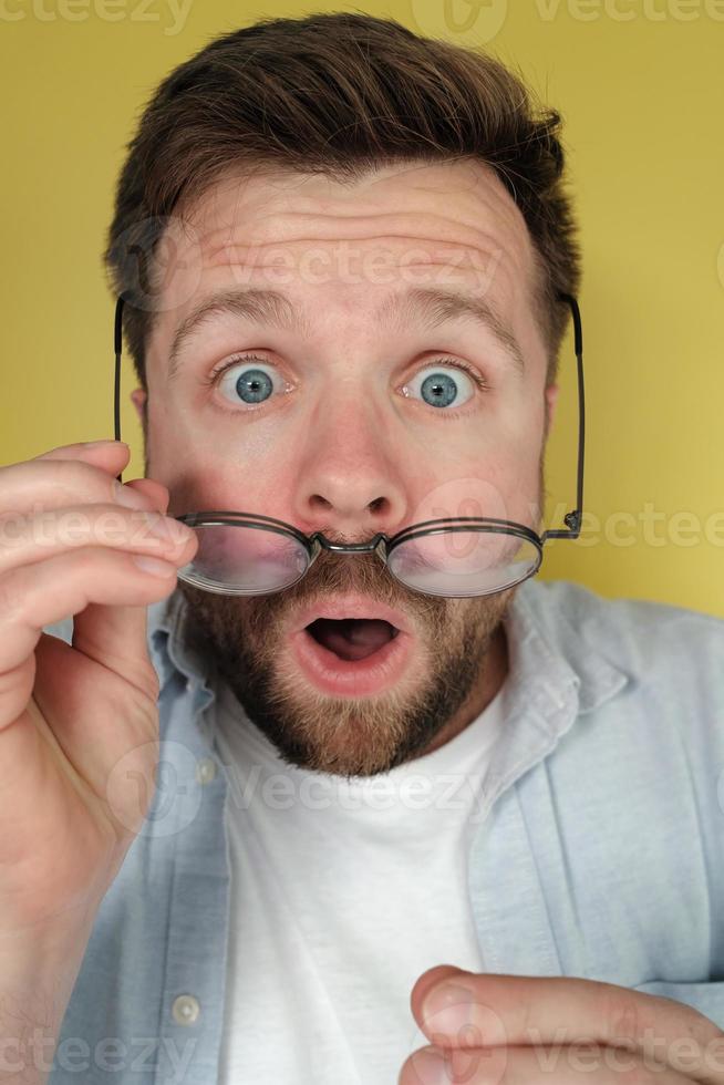 Man with a shocked expression holds his glasses, which he took off in surprise. Close-up. photo