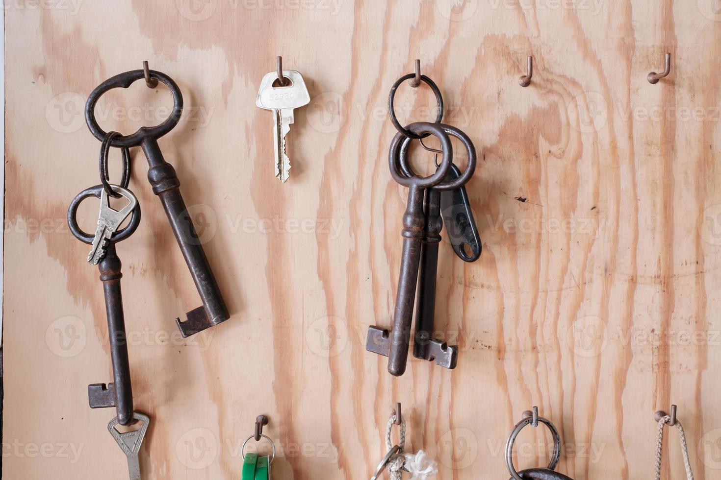 Various vintage and modern door keys hang on hooks on a wooden board. photo
