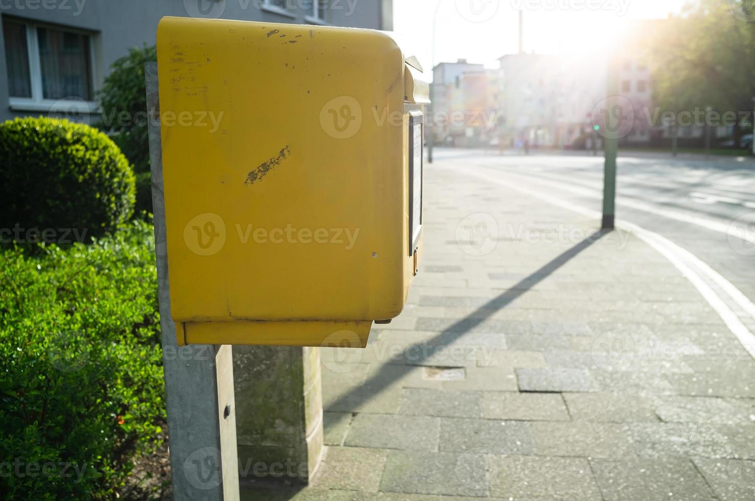 Yellow mailbox for letters on the street of a provincial town, in the sunlight. photo