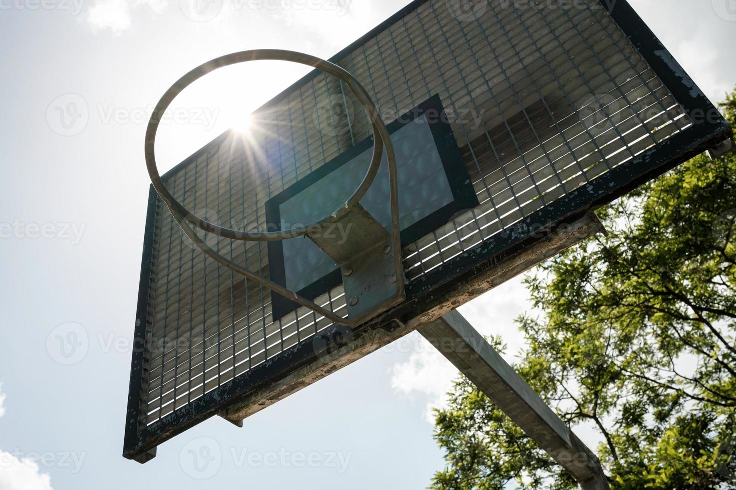 canasta de baloncesto sobre fondo de sol, cielo y árbol. campo de deportes al aire libre. concepto de un estilo de vida activo. vista inferior. foto